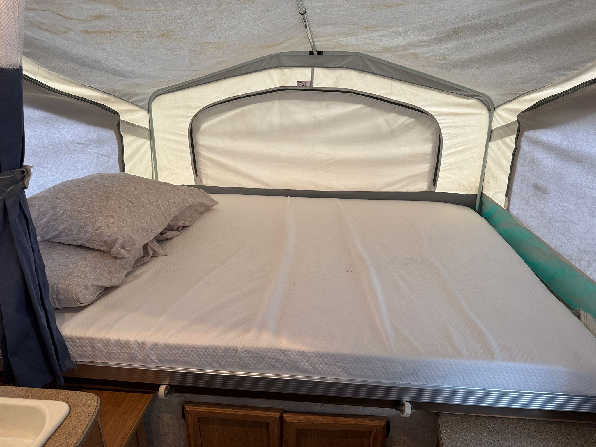 RV rental pop-up camper bed with white mattress, pillows. Canvas interior, "EXIT" sign above, ready for your camping trip.. Forest River Palomino Y-Series 2010
