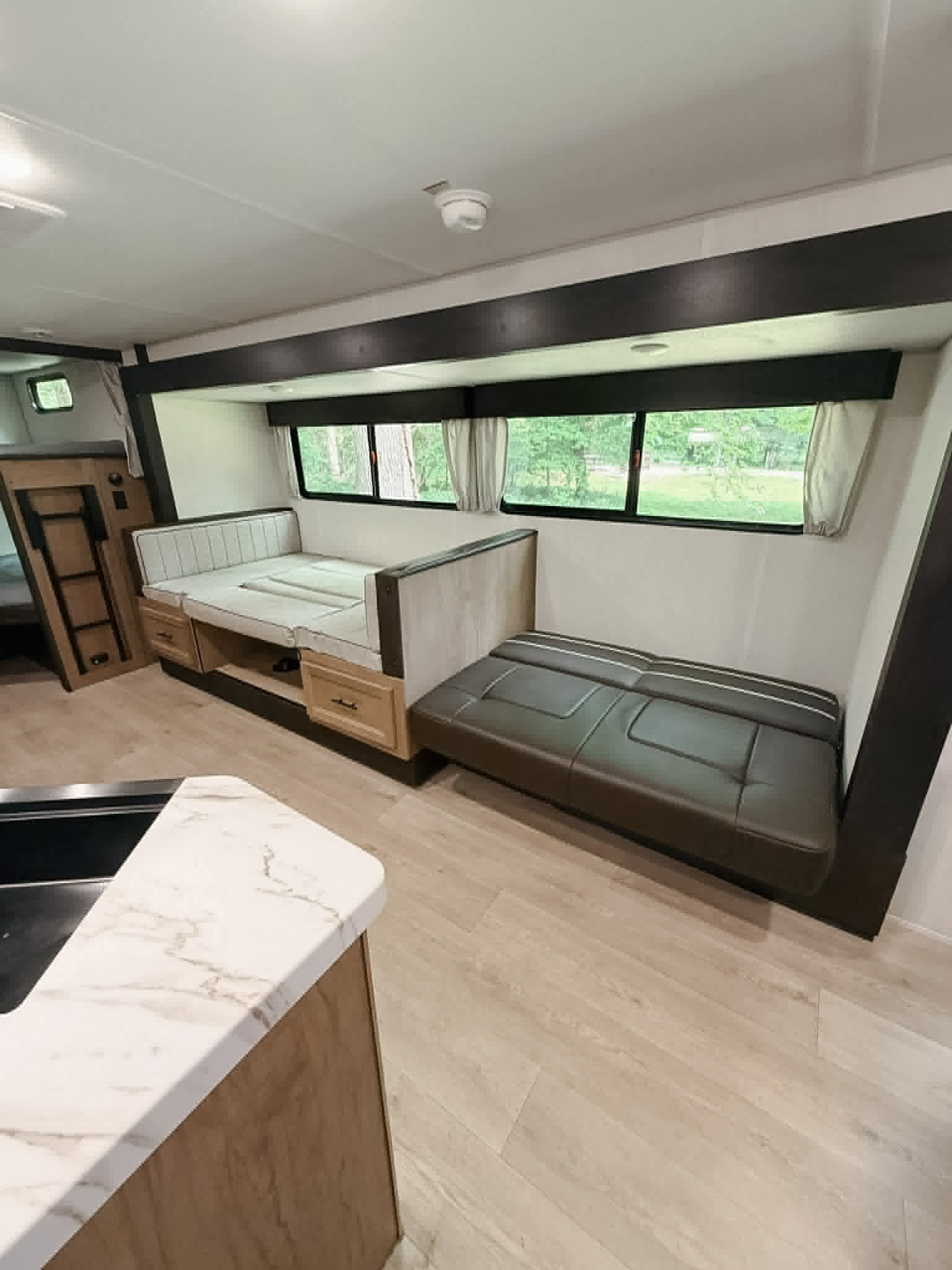 Cozy RV rental interior: light dinette, bunk beds, convertible sofa, & kitchen area, all with light wood-look floors.. Forest River Cherokee Grey Wolf 2025