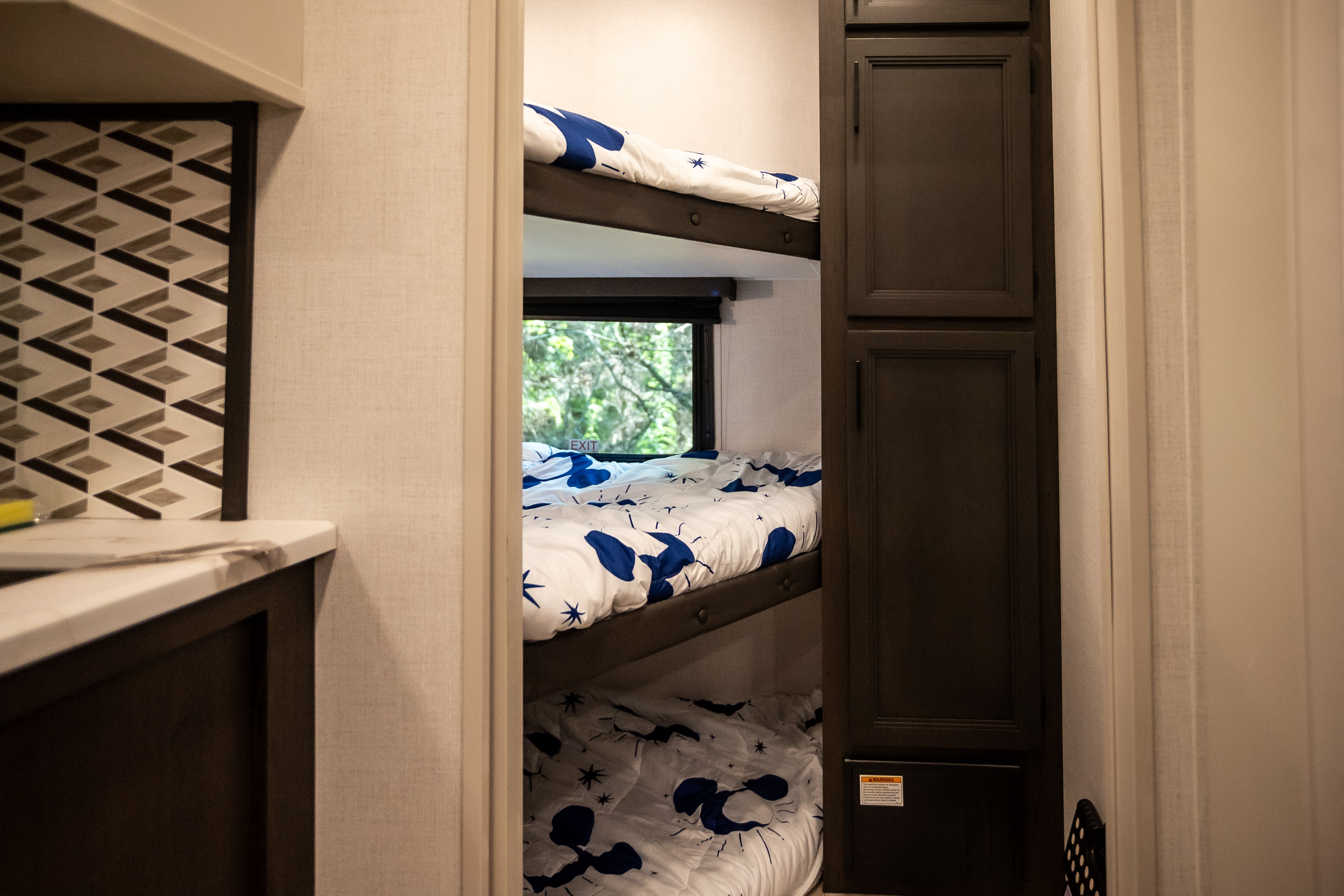 Cozy RV rental bunk beds with a view of nature, complete with white and blue patterned bedding and storage cabinets.. Keystone RV 27SBH 2026