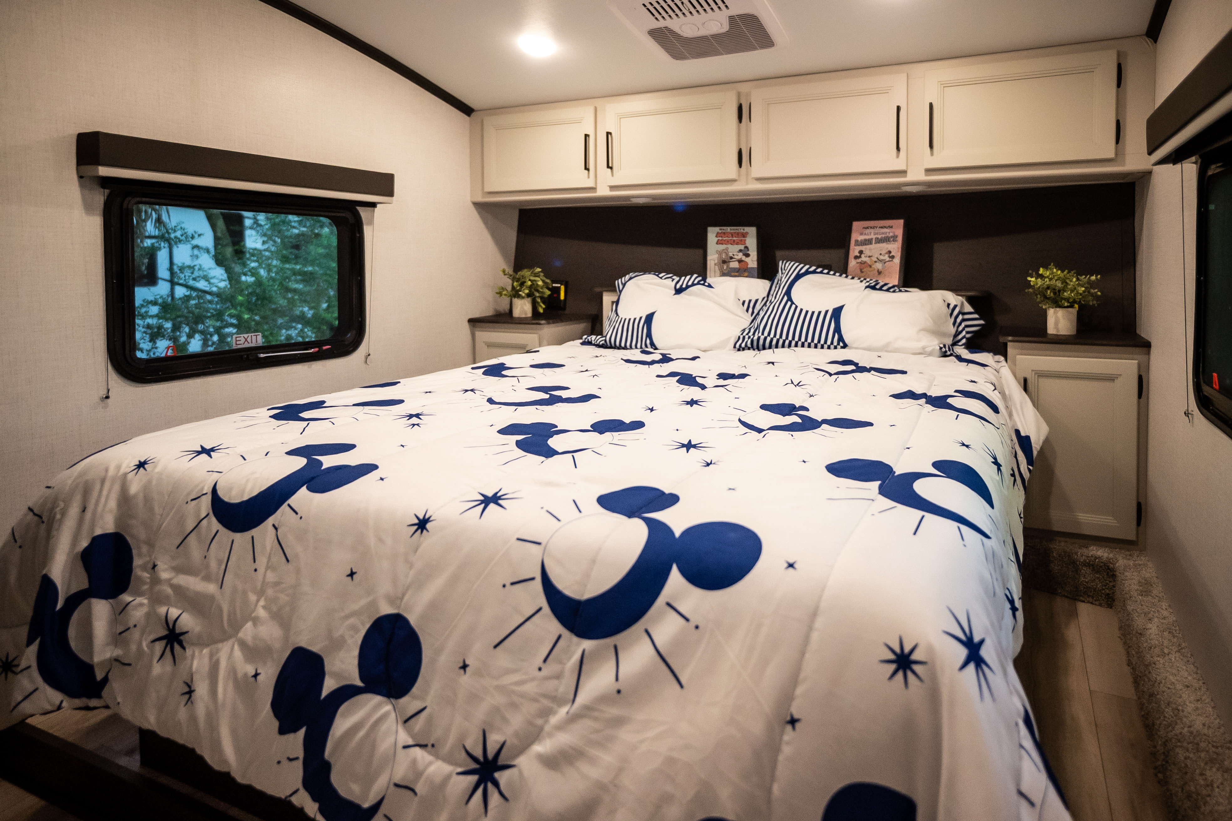 RV rental bedroom features a cozy bed with fun Mickey Mouse bedding, overhead cabinets, and a window for natural light.. Keystone RV 27SBH 2026