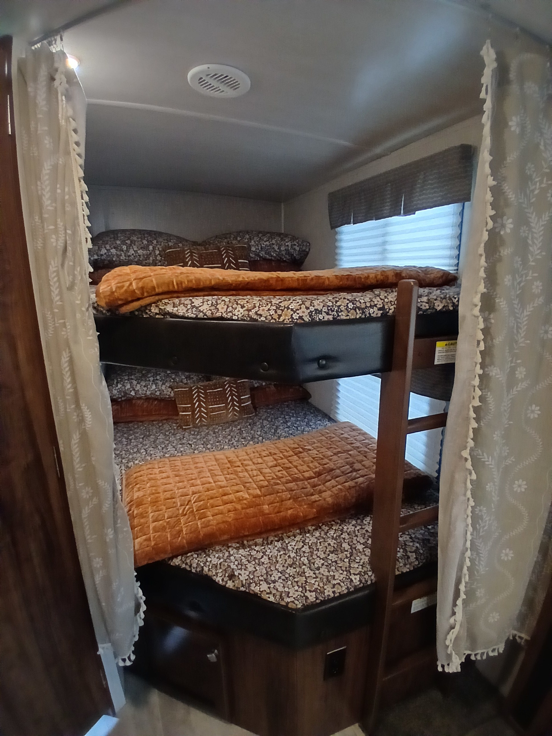 Cozy RV rental bunk beds with patterned bedding, orange blankets, and decorative curtains, ideal for families.. Heartland RVs Wilderness 2018