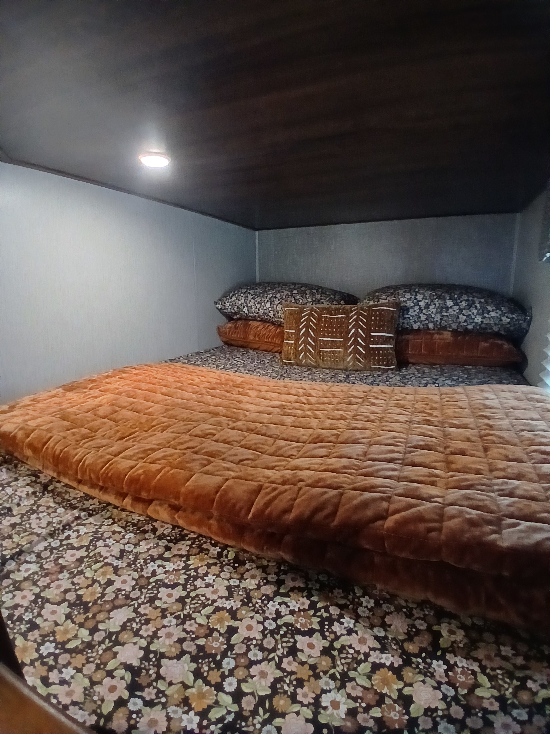Cozy RV rental sleeping area featuring a bed with floral sheets, quilted rust-colored blanket, and decorative pillows.. Heartland RVs Wilderness 2018