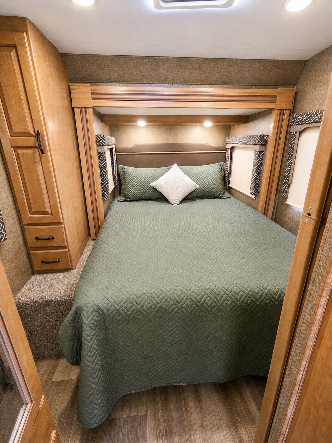 This RV rental features a cozy bedroom with a quilted green bedspread, wood cabinetry, and bedside lighting.. Thor Four Winds 2018