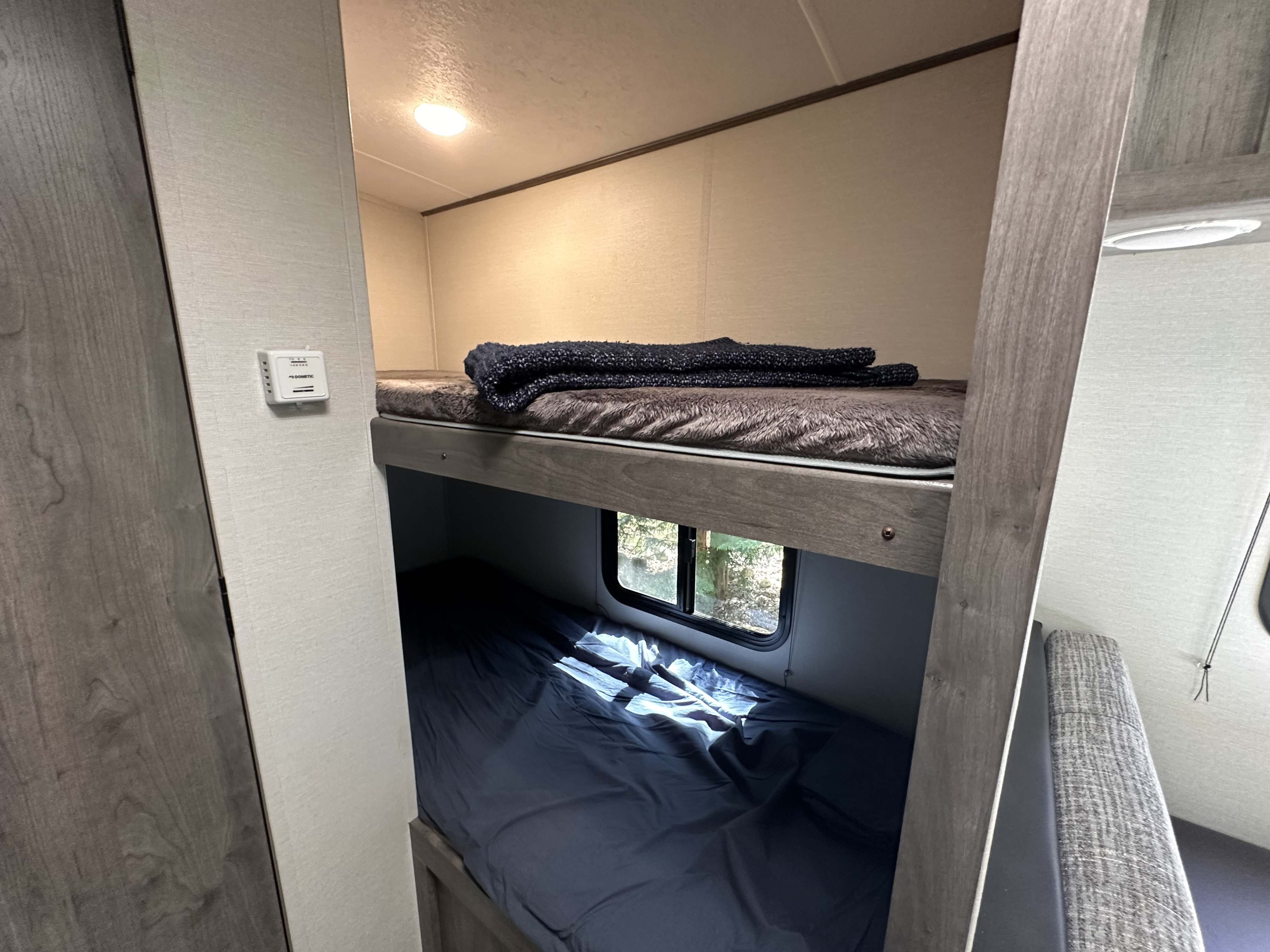 Cozy RV rental bunk area features upper and lower bunks with bedding, a wall-mounted thermostat, and a window.. Coachmen Apex Nano 2021