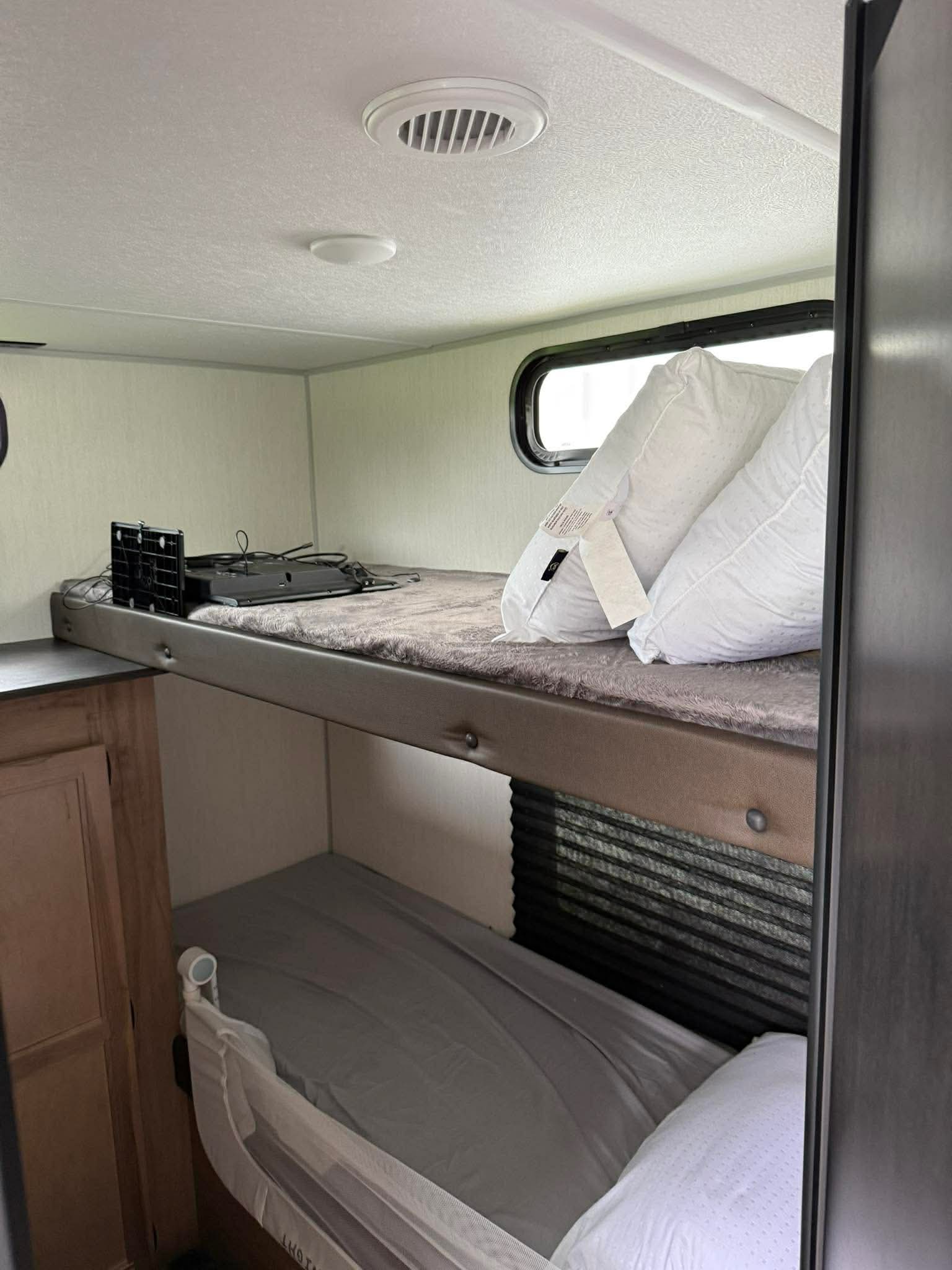 Inside an RV rental: view of stacked bunk beds. The top bunk has pillows and a TV, while the lower bunk features a child safety rail.. Forest River Cherokee Grey Wolf 2025