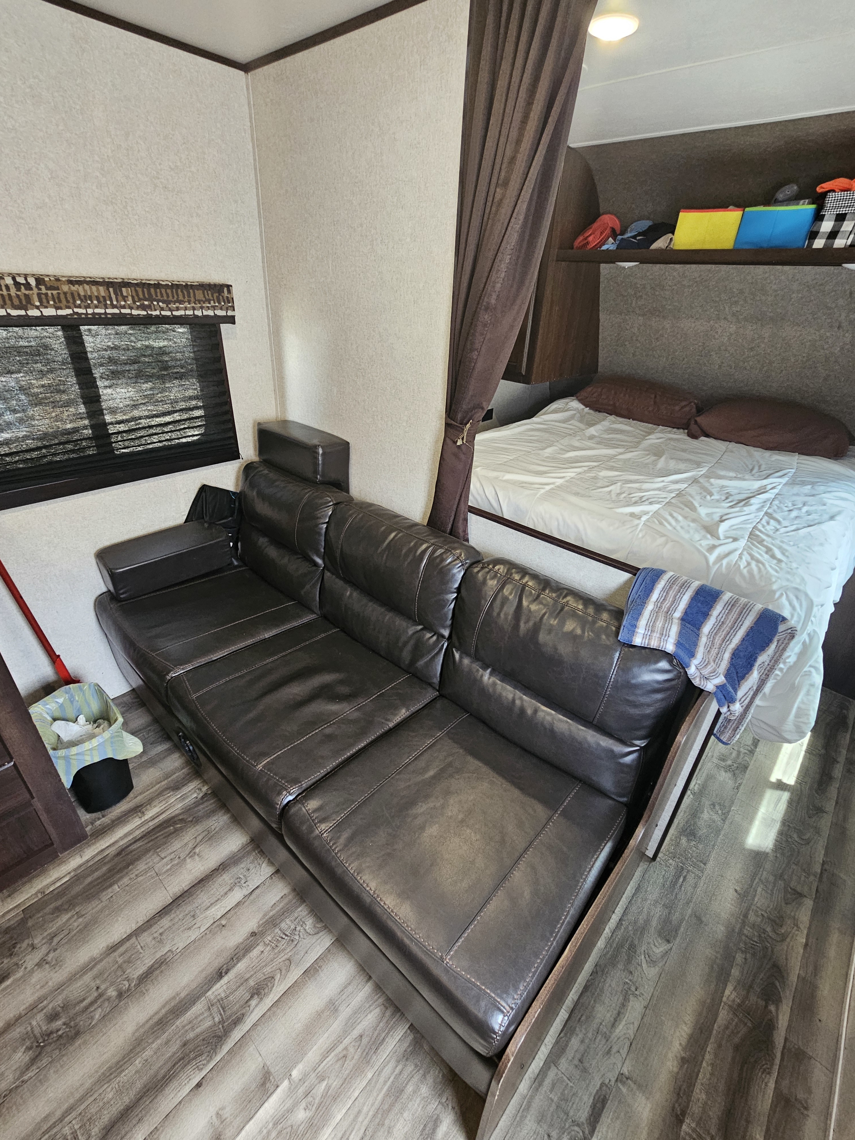 RV rental interior: A dark leather sofa in the living area, leading to a bed with white linens behind a privacy curtain.. Jayco Jay Flight SLX Rocky Mountain Edition 2018