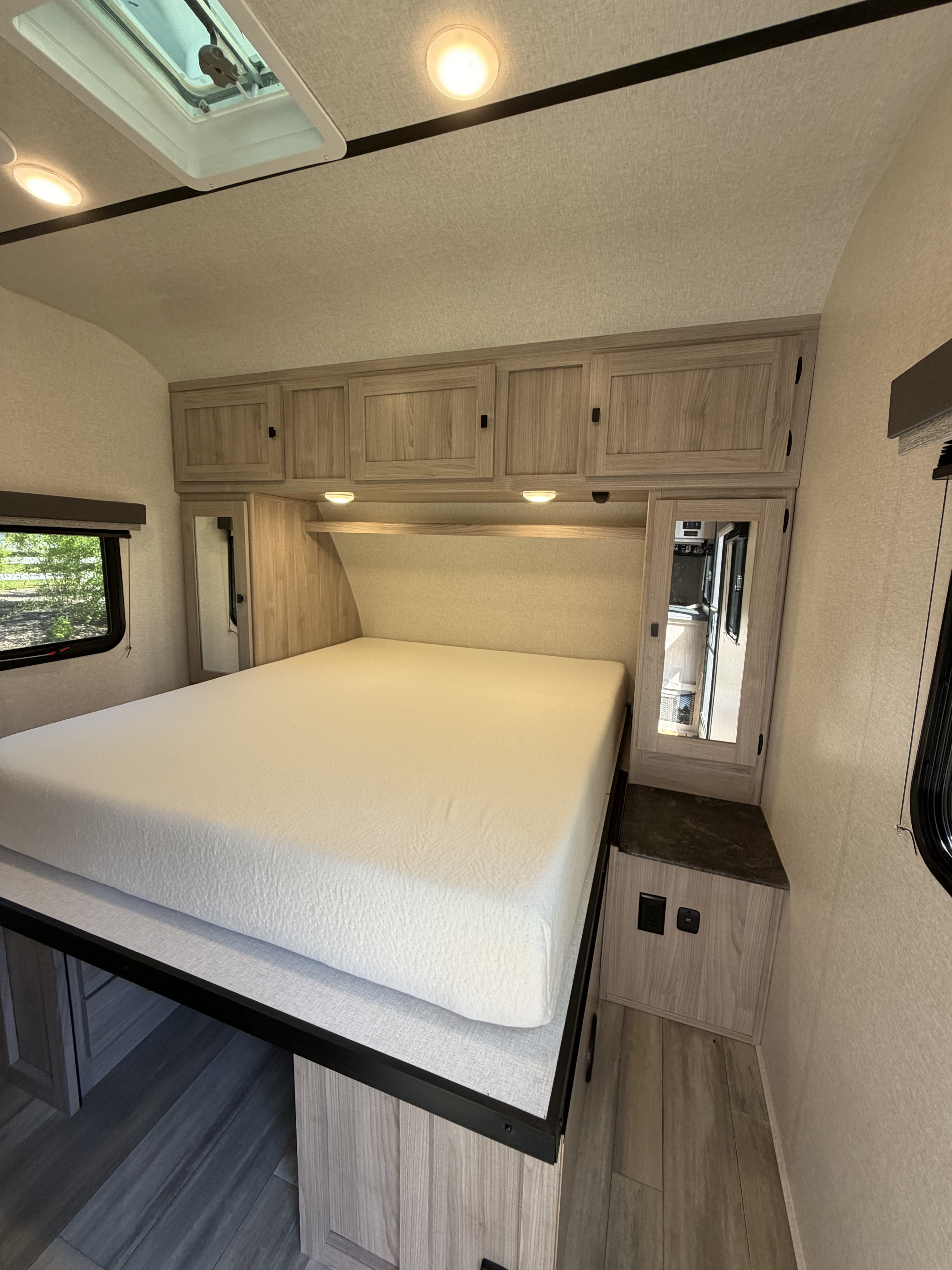 Bright RV rental bedroom features a large white bed, light wood cabinets, and windows with scenic views, perfect for an RV trip.. Coachmen 2963BH 2023