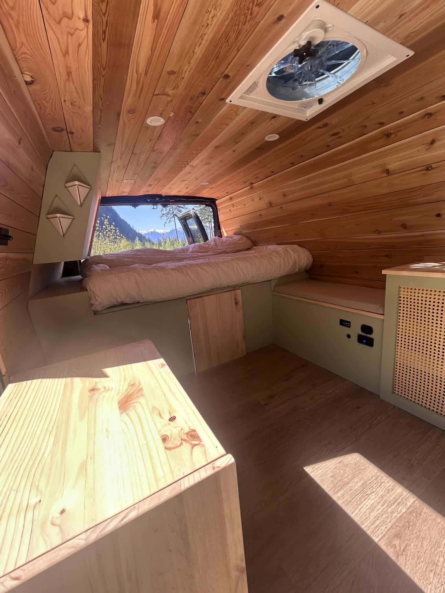 Custom wood-paneled van interior for an RV rental, featuring a cozy bed, seating, and a stunning mountain view.. Ford Econoline 2005