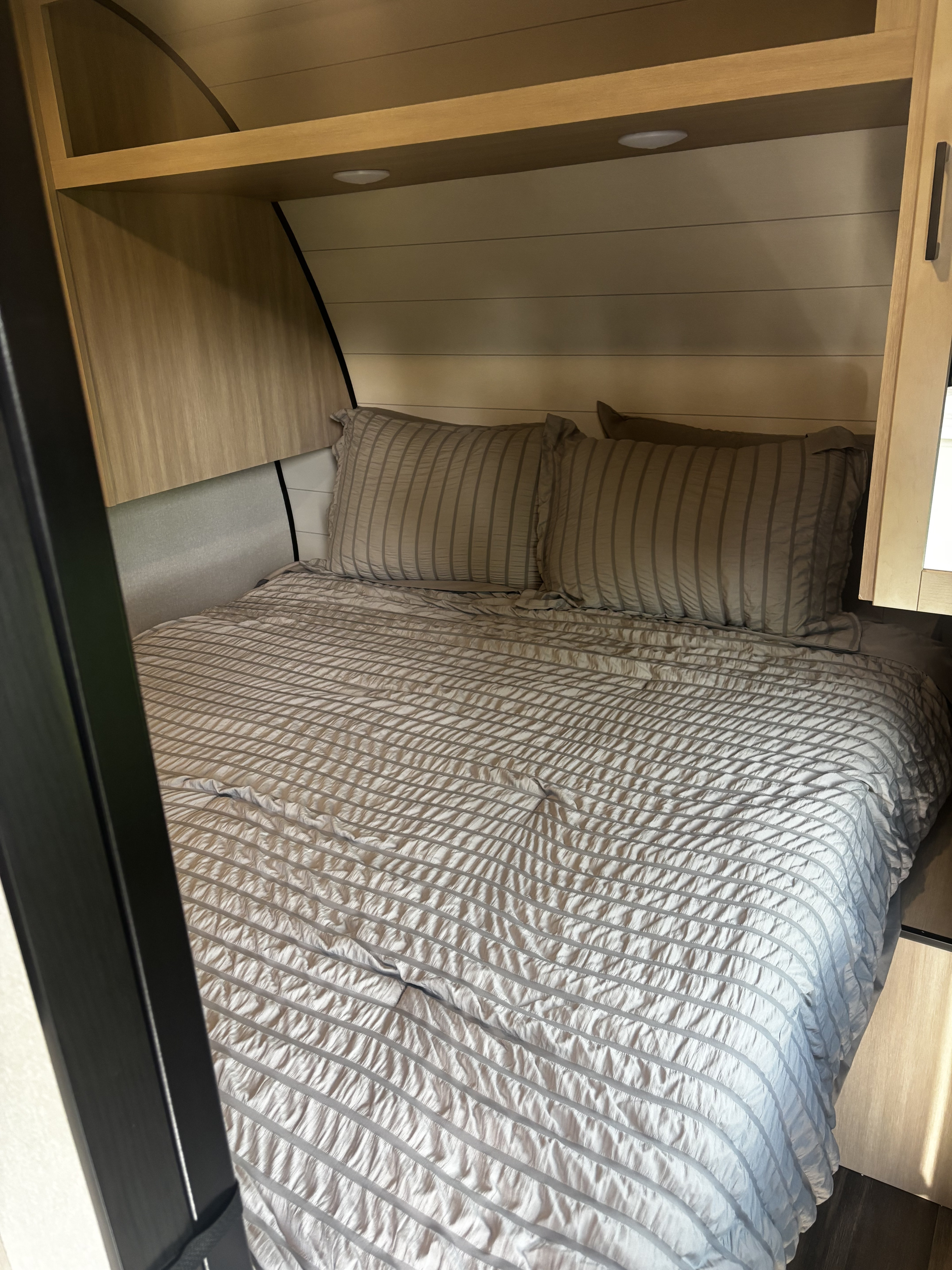 Cozy RV rental bedroom with striped bedding, pillows, and built-in wooden storage above. Ideal for travel.. Highland Ridge RV Colt 2026