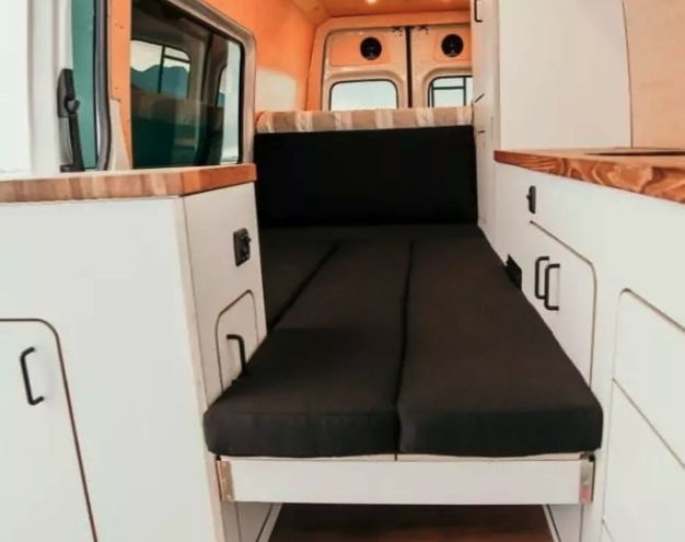 Explore this clean, compact camper van interior, perfect for your next RV rental. Features a comfy bed & smart storage.. Mercedes-Benz Sprinter 2022