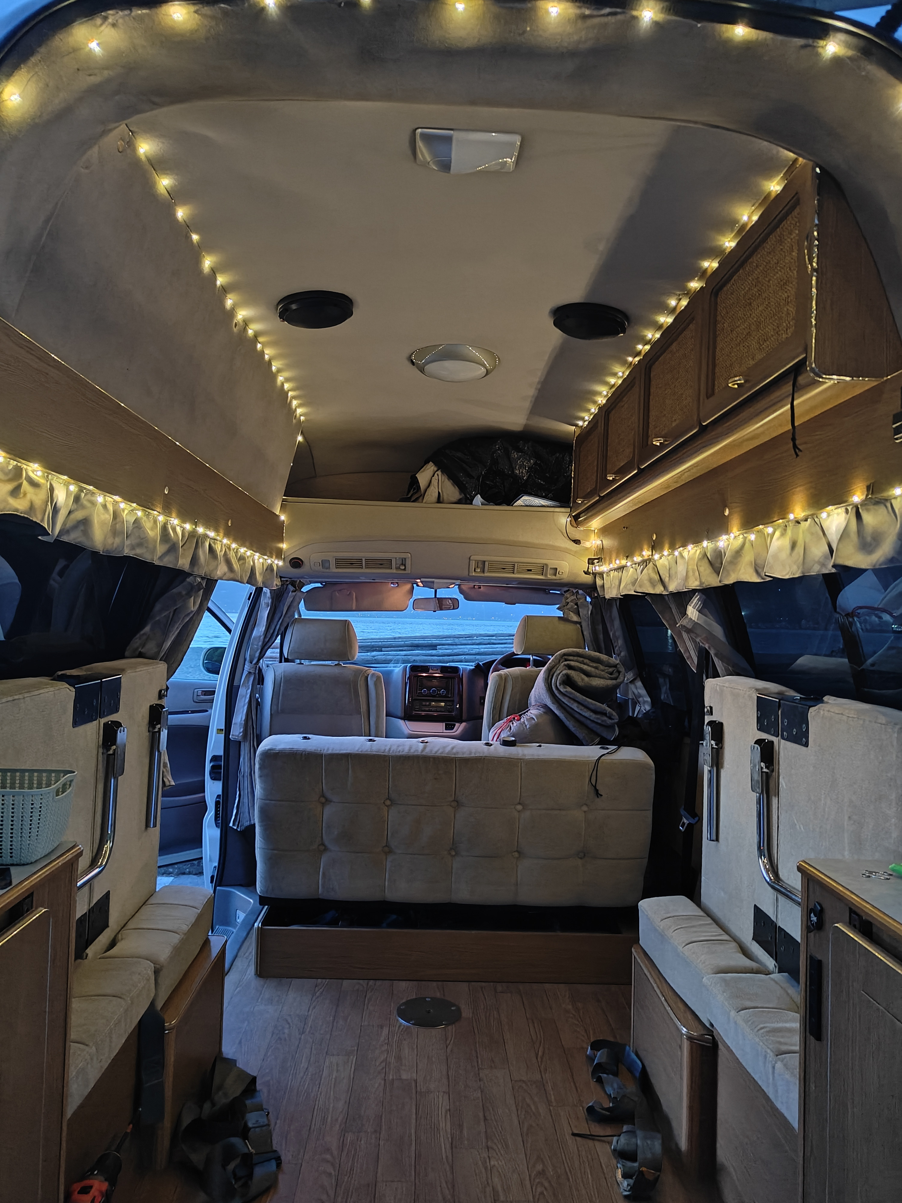 Cozy rv rental camper van interior with string lights, wood floor, and adaptable seating, perfect for an adventure.. Toyota Hiace 4WD 2004