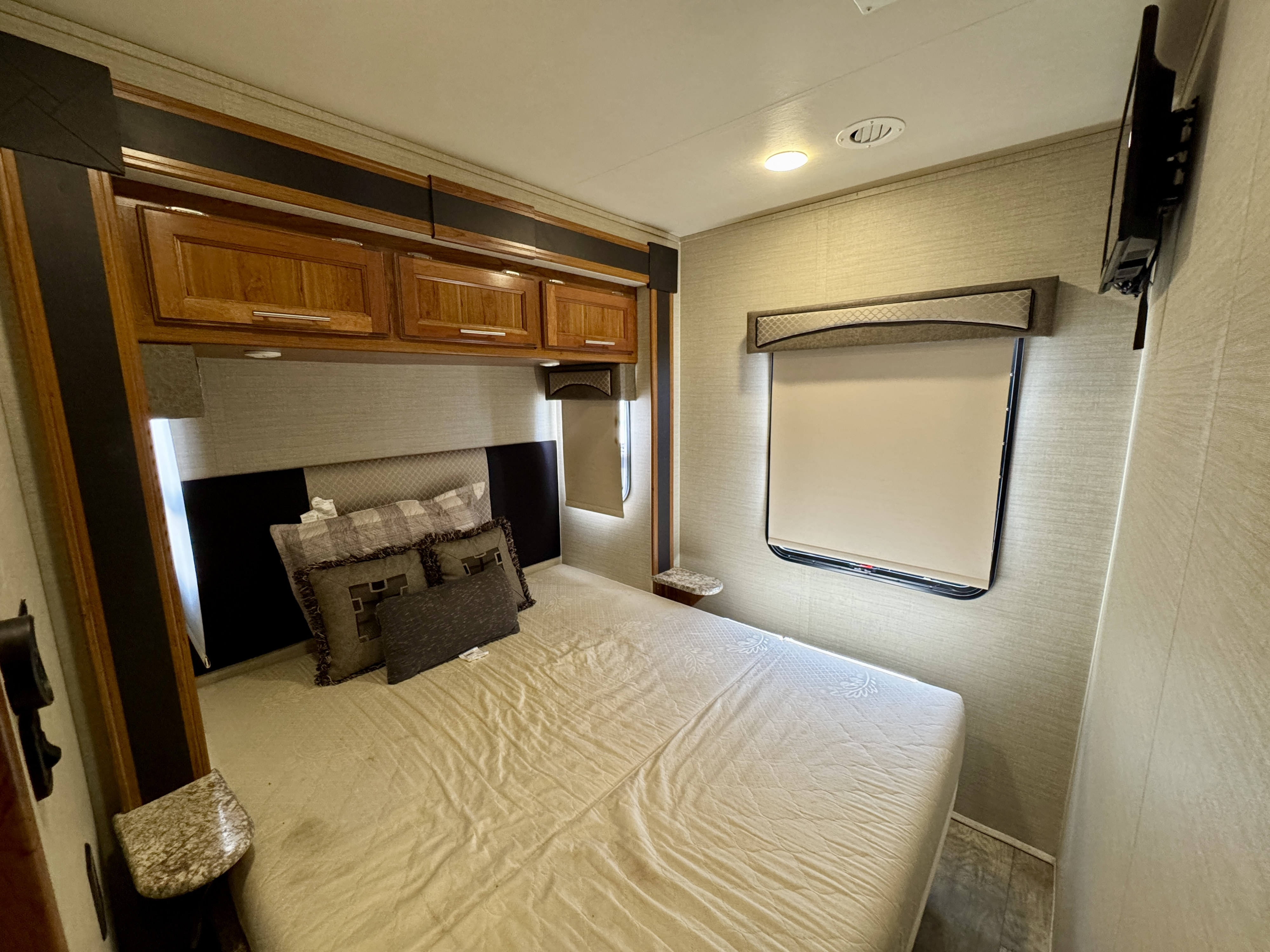 Cozy RV rental bedroom featuring a comfy bed, overhead wooden cabinets, windows with pull-down blinds, and a wall-mounted TV.. Jayco Alante 2017