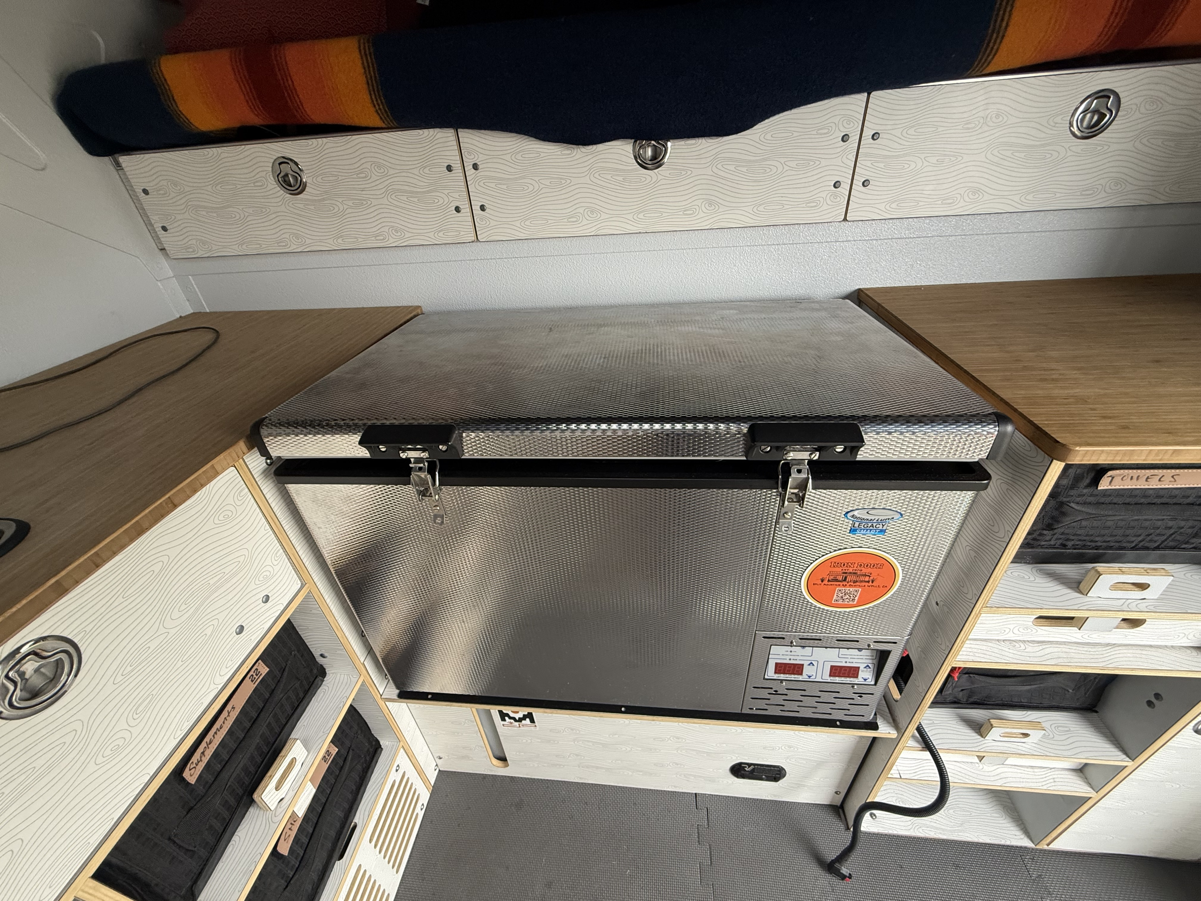 RV rental van interior showcases a portable fridge, sleek patterned storage cabinets, and an overhead sleeping area.. Dodge Ram Ram 2022