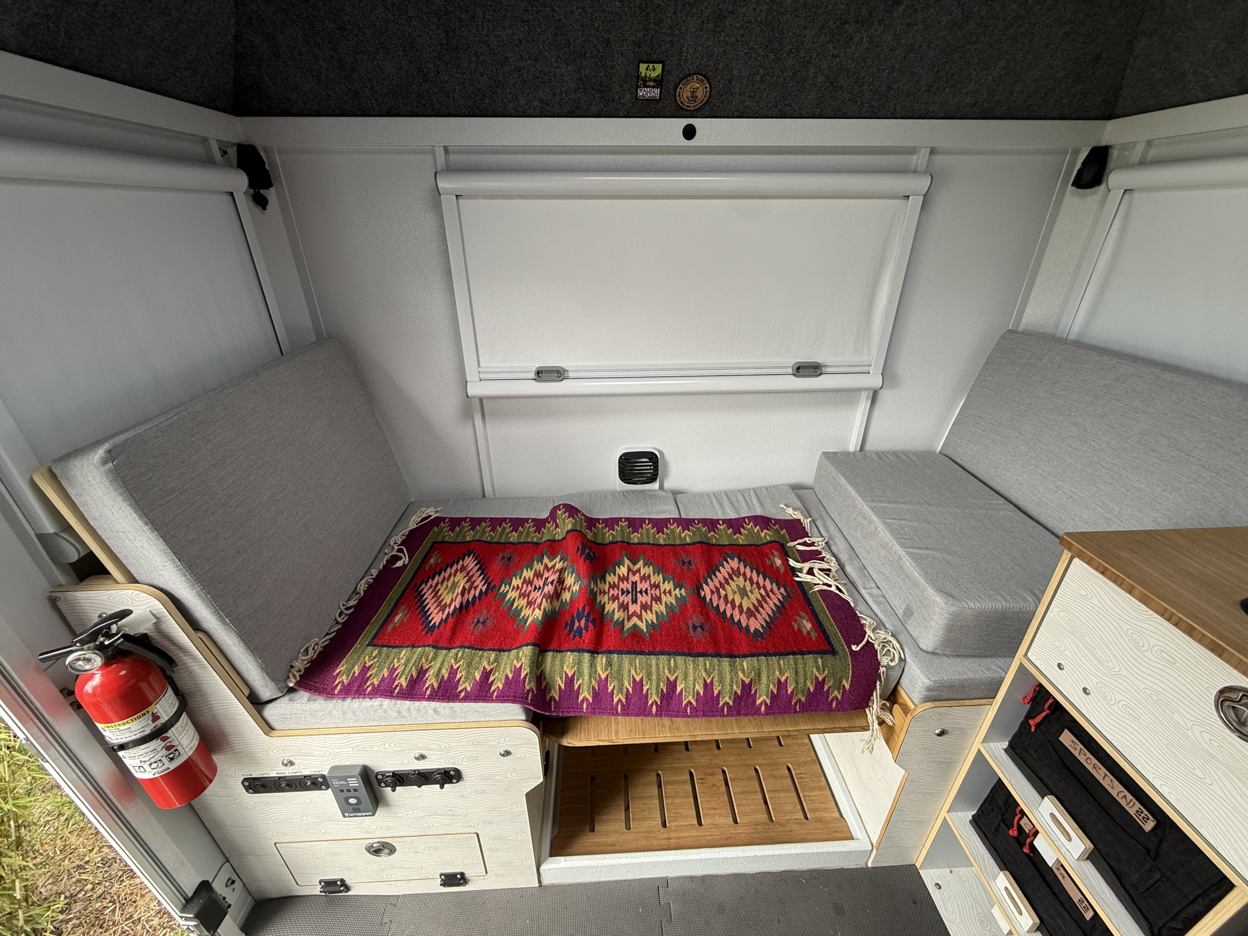 Inside an rv rental: grey benches, colorful rug, fire extinguisher, and controls. Compact and functional space.. Dodge Ram Ram 2022