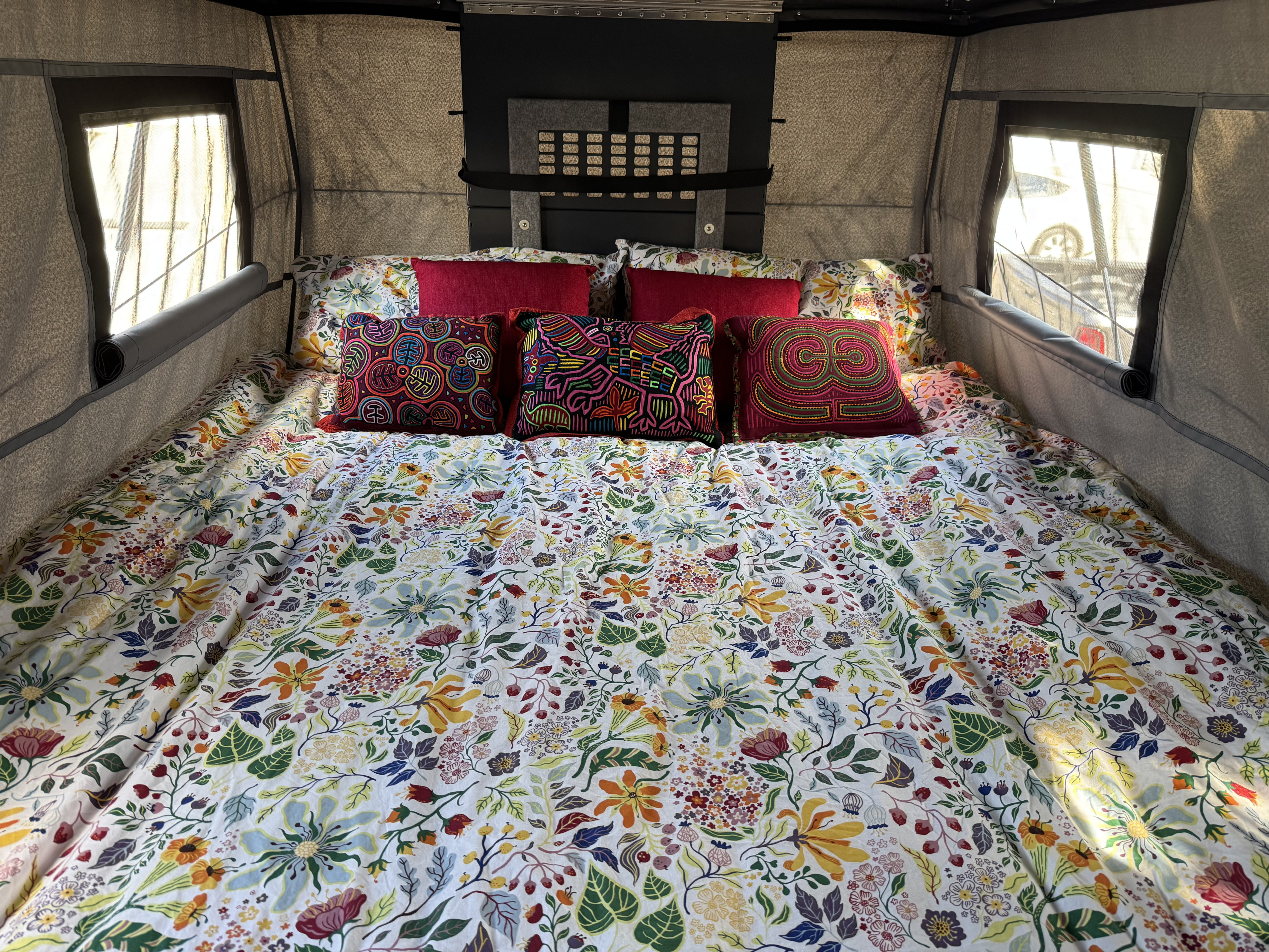 Inviting RV rental interior with a comfortable bed, vibrant floral duvet, and colorful embroidered pillows by screened windows.. Toyota Tundra 2025