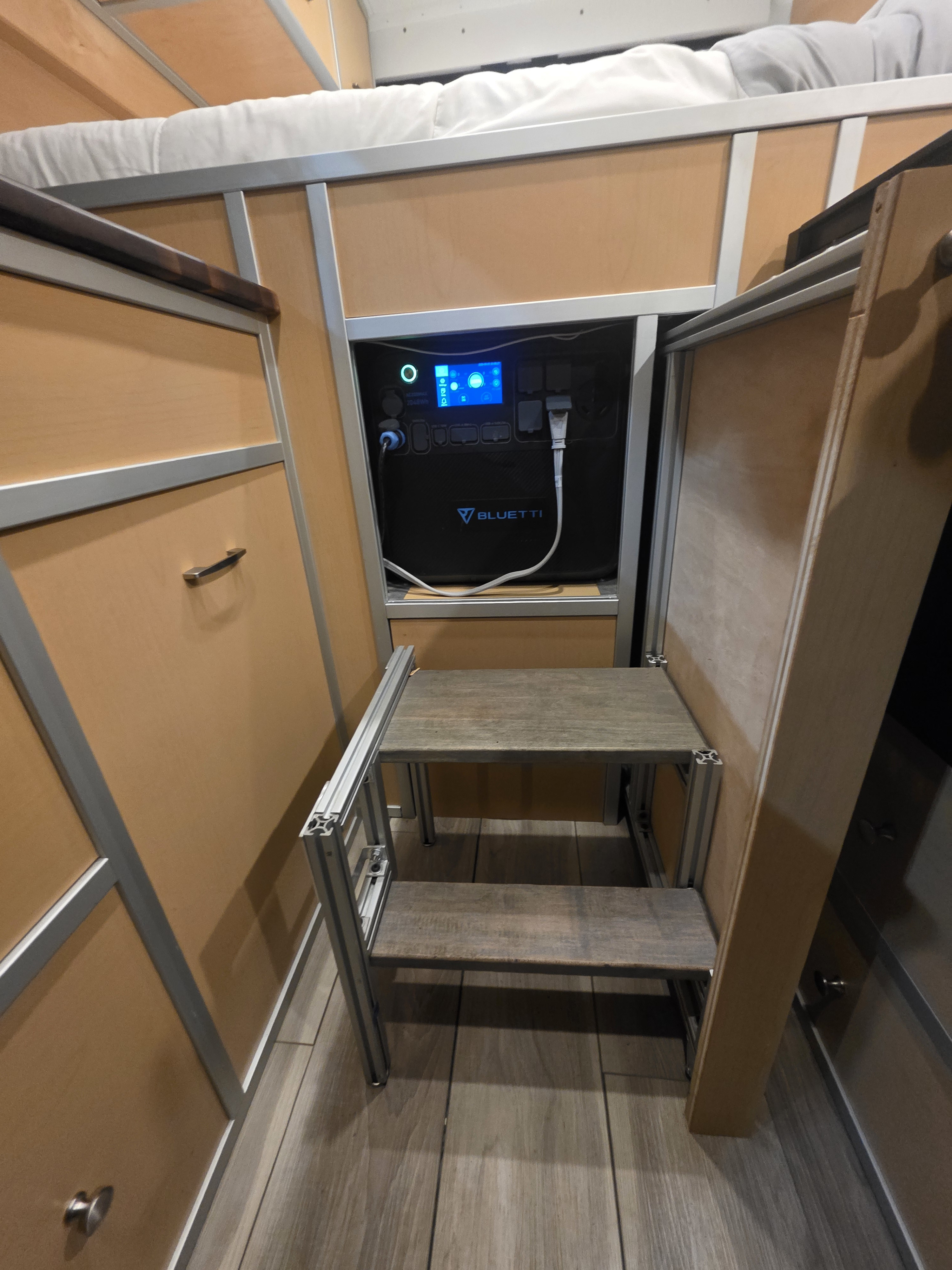Bluetti power station, plugged in and integrated into a compact RV rental interior, with a custom two-step ladder & bunk bed.. Custom Built Avantgarde 2013