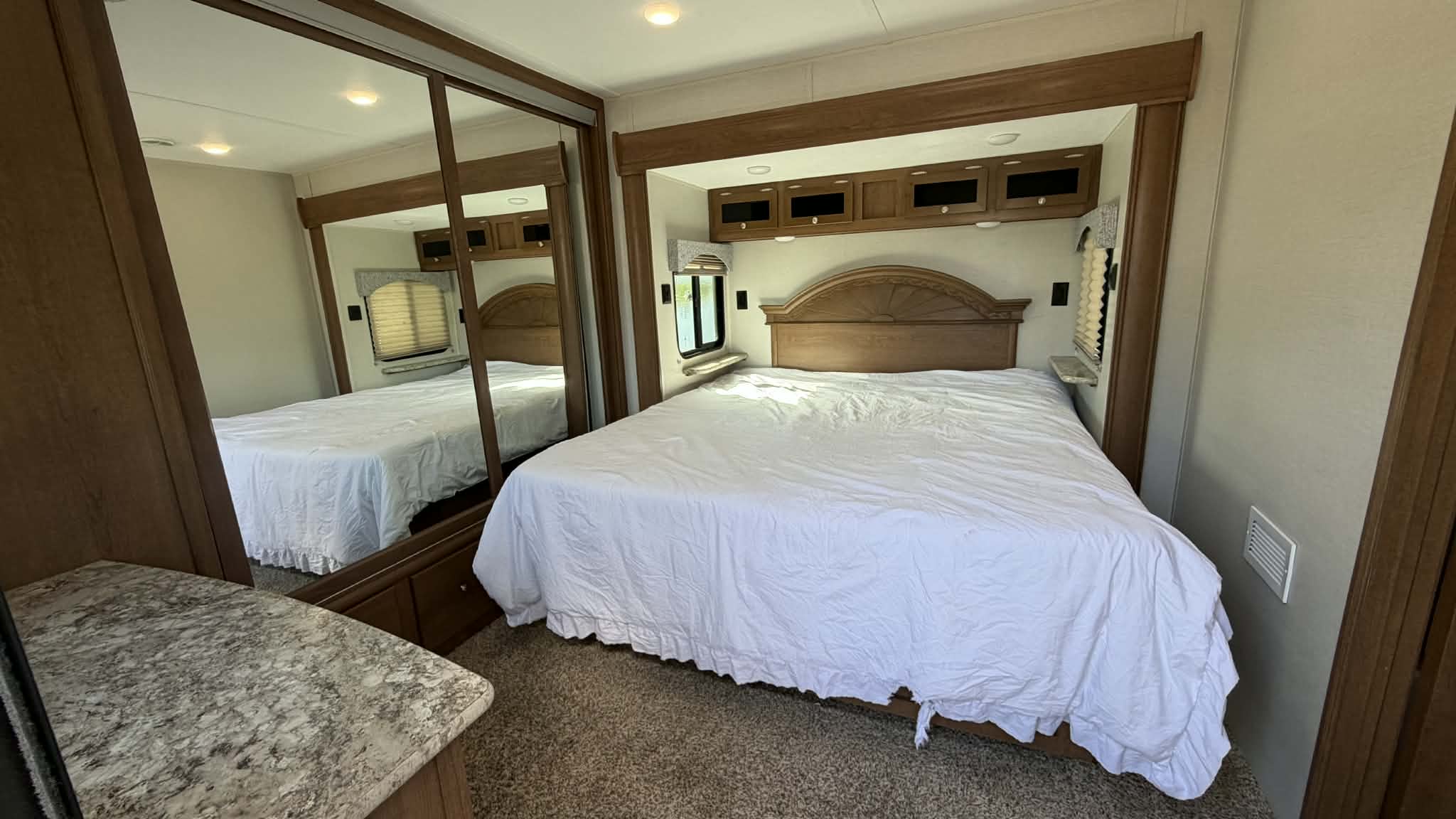 Bright RV rental bedroom with a large bed, mirrored closet, and wooden overhead cabinets. Enjoy cozy nights on the road.. 5CZ200R34P1228760 2023 camper 2023