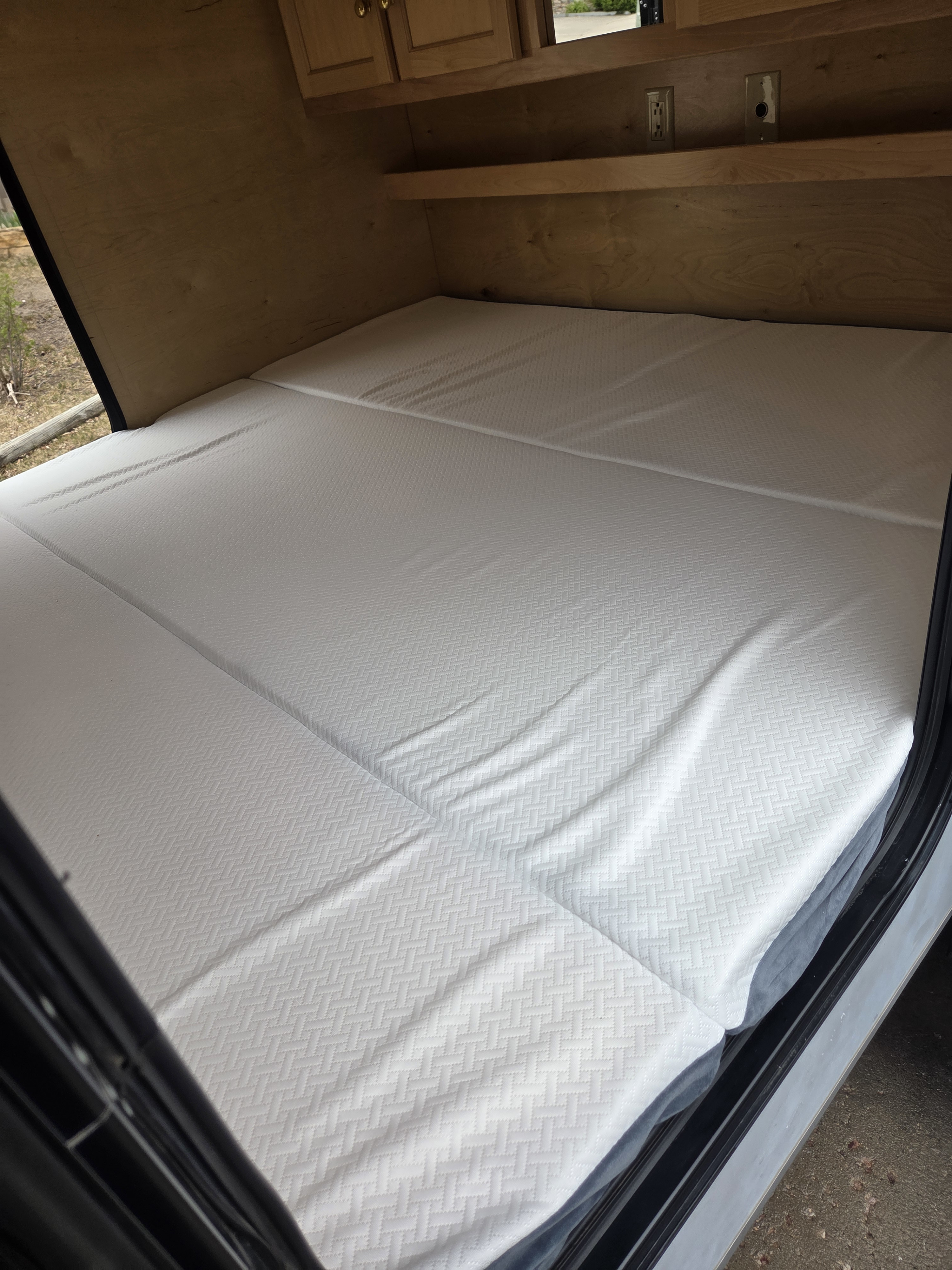 Cozy RV rental sleeping area featuring a segmented white mattress, wooden walls, shelves, and cabinets for comfort.. Little Guy Little Guy Trailer 2013