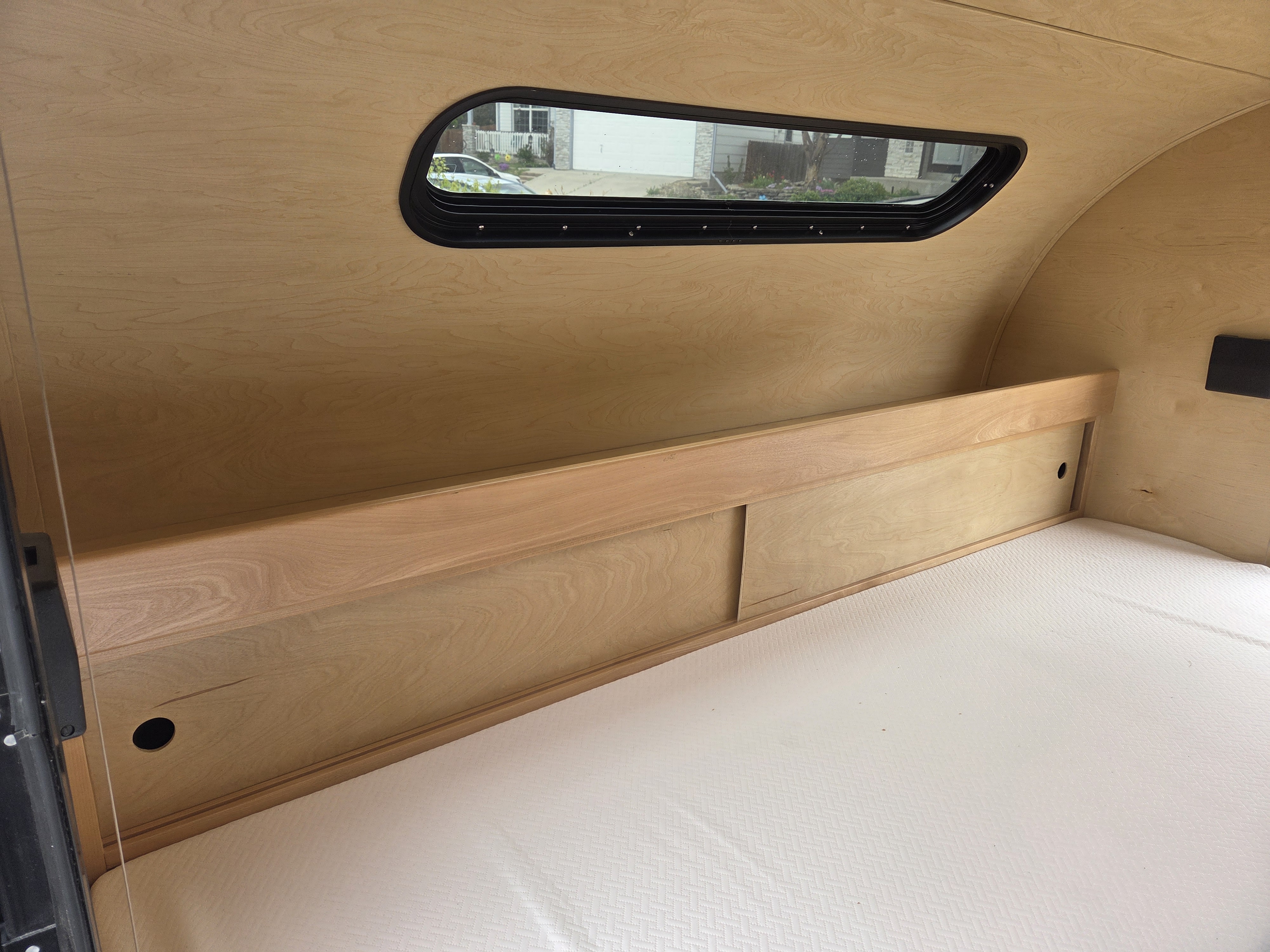 Cozy RV rental interior featuring light wood paneling, a comfy mattress, built-in storage, and a scenic window view.. Little Guy Little Guy Trailer 2013