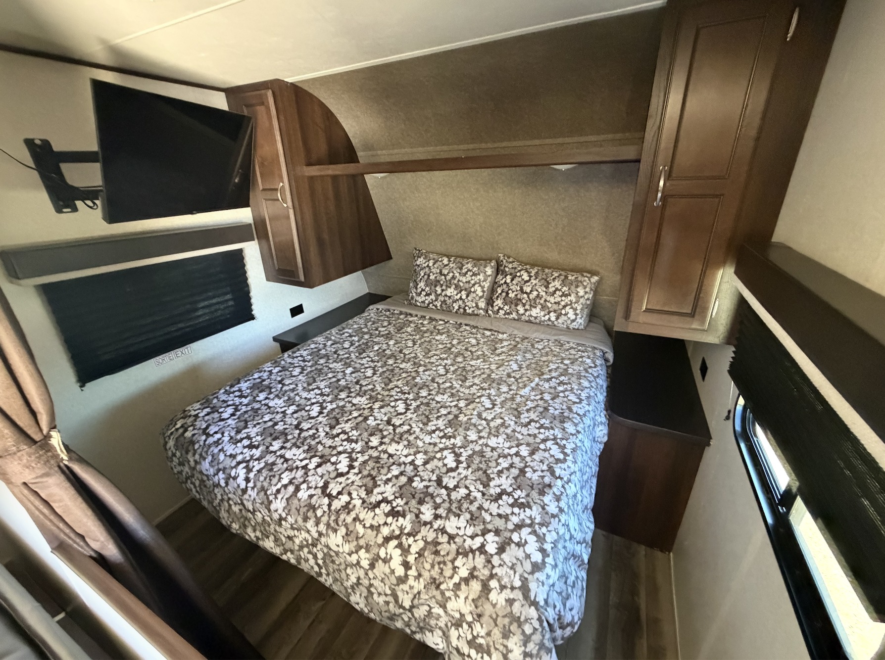 Cozy RV rental bedroom featuring a floral bedspread, wall-mounted TV, overhead storage, and window. Ideal for travel.. Jayco Jay Flight SLX 2018