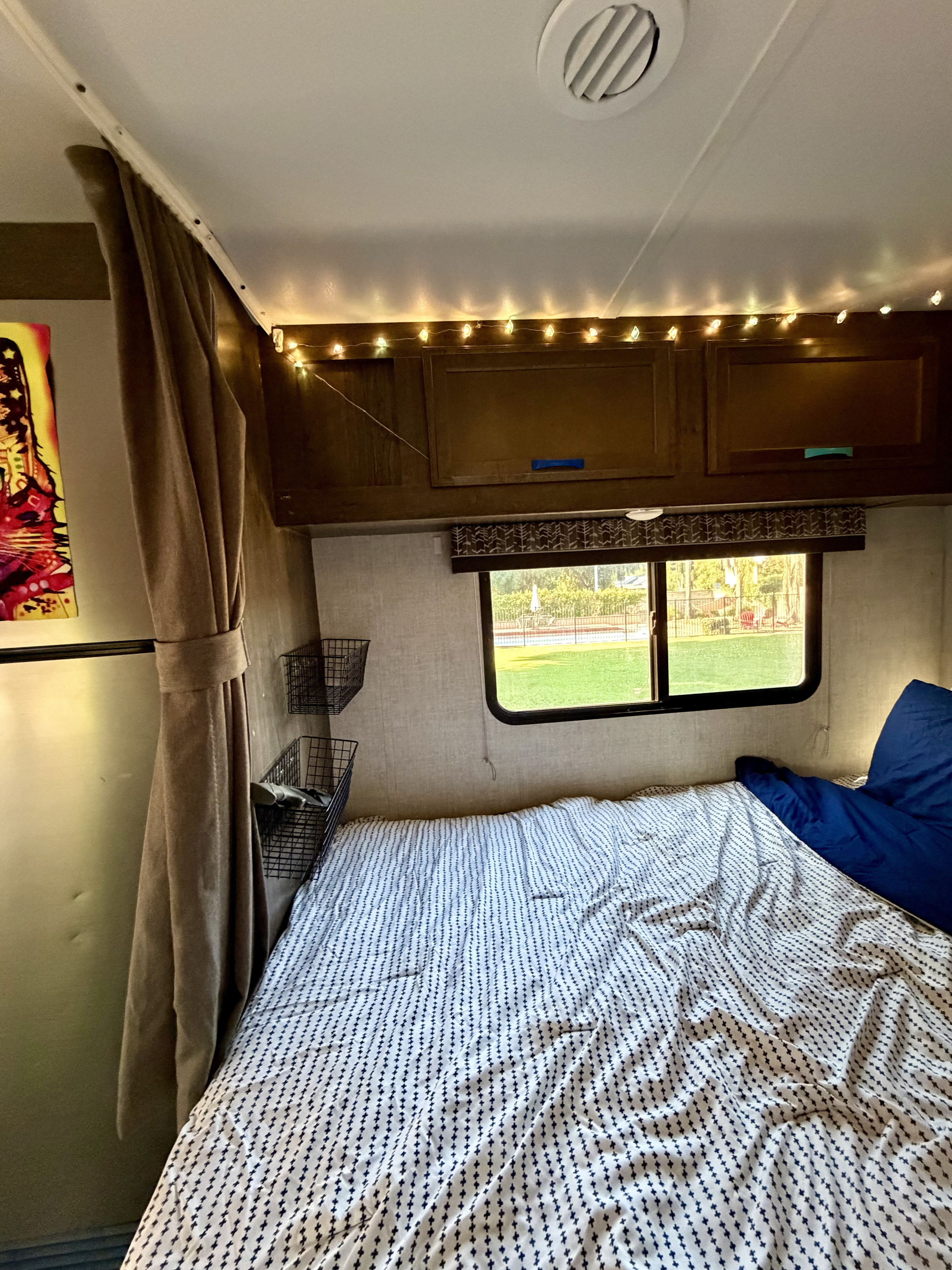 Cozy RV rental interior with a comfy bed, string lights, storage baskets, and a view to green grass.. Gulf Stream Conquest 2023