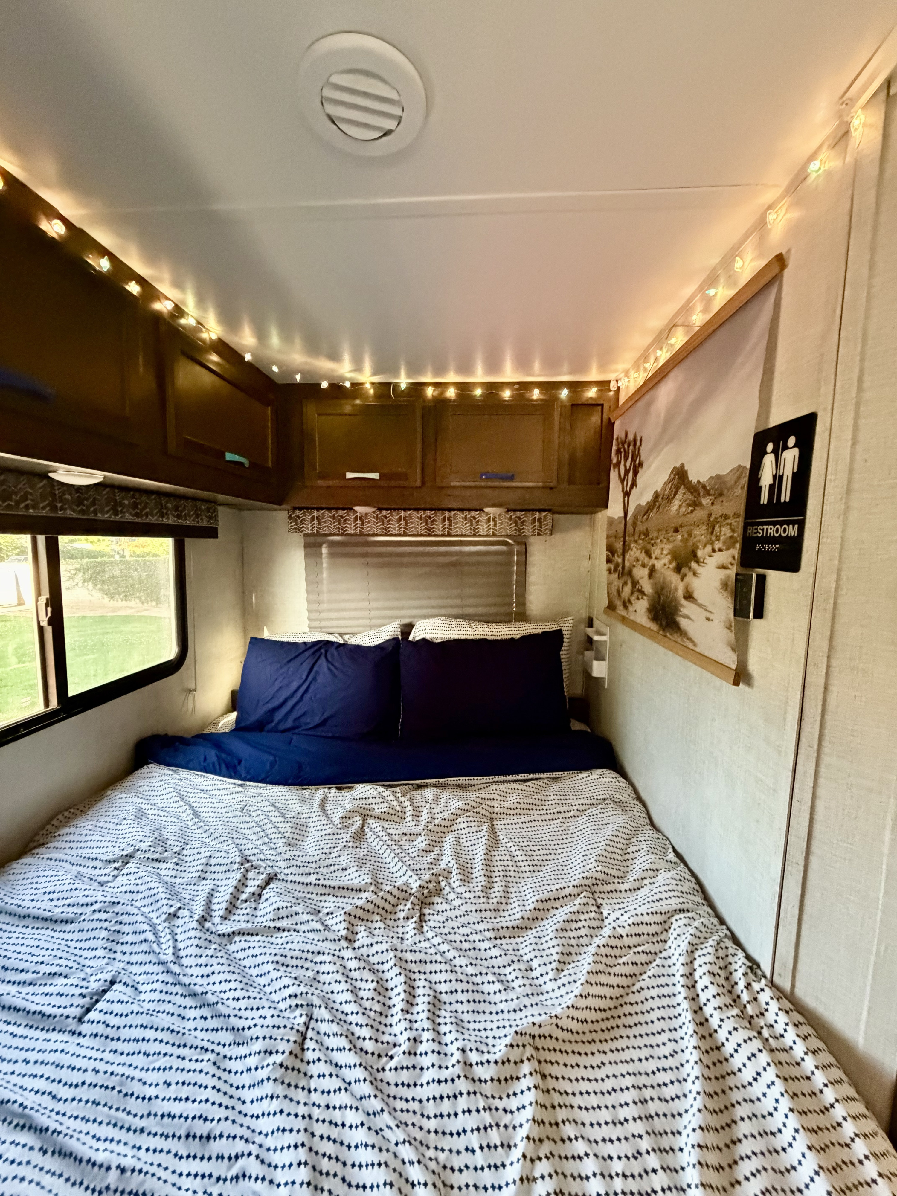 Cozy RV rental bedroom with string lights, a patterned duvet, and a desert art print, offering a comfortable interior.. Gulf Stream Conquest 2023