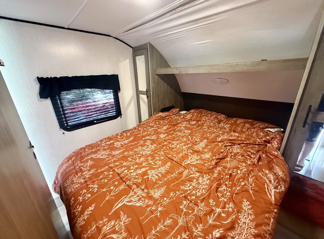 RV rental bedroom featuring a bed with vibrant orange floral comforter, window, and built-in storage, ready for adventure.. Heartland RVs Pioneer 2023