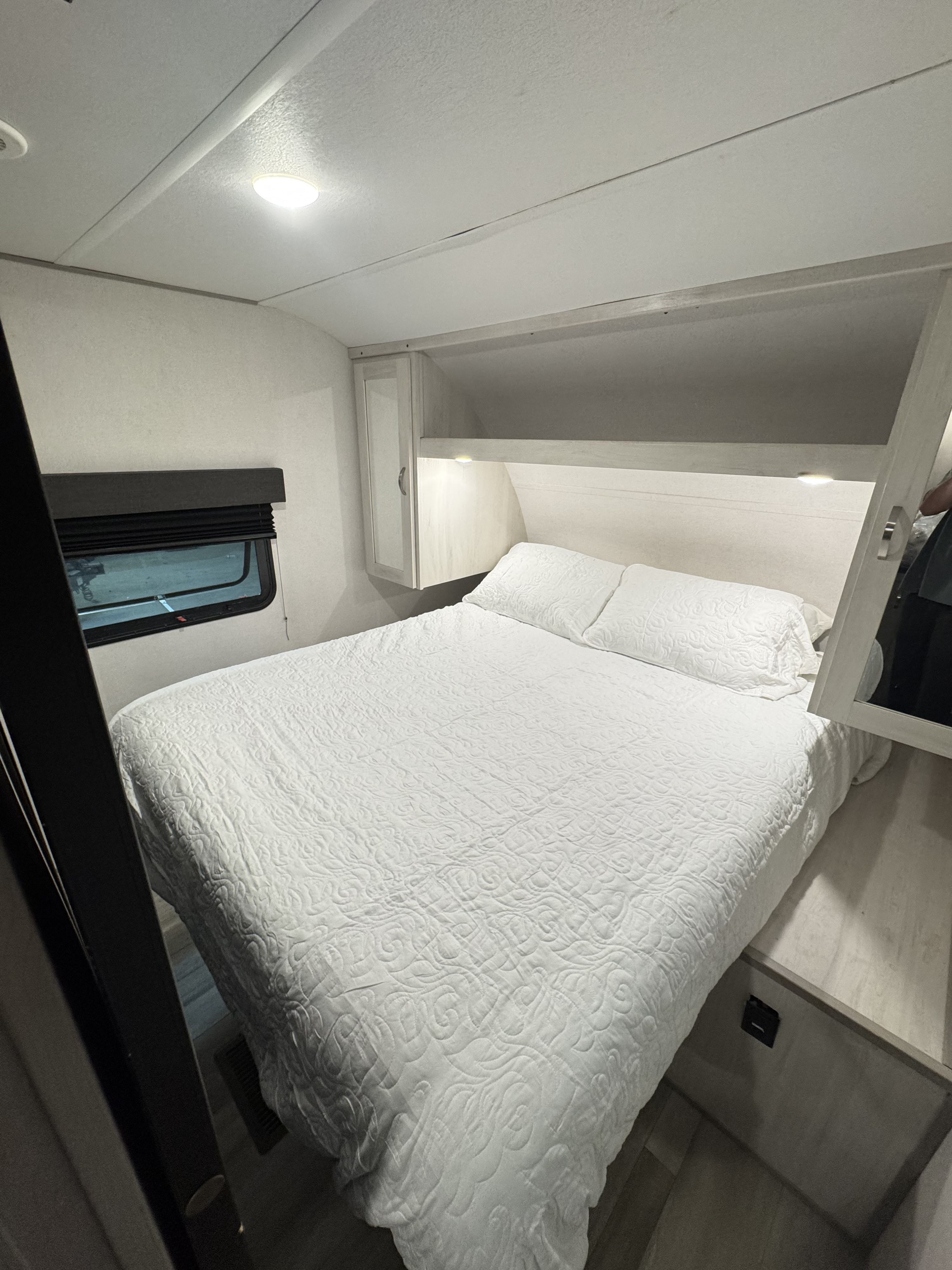 Cozy and bright RV rental bedroom featuring a white quilted bed, built-in storage, and window. Ideal for travelers.. Forest River Tracer 2021