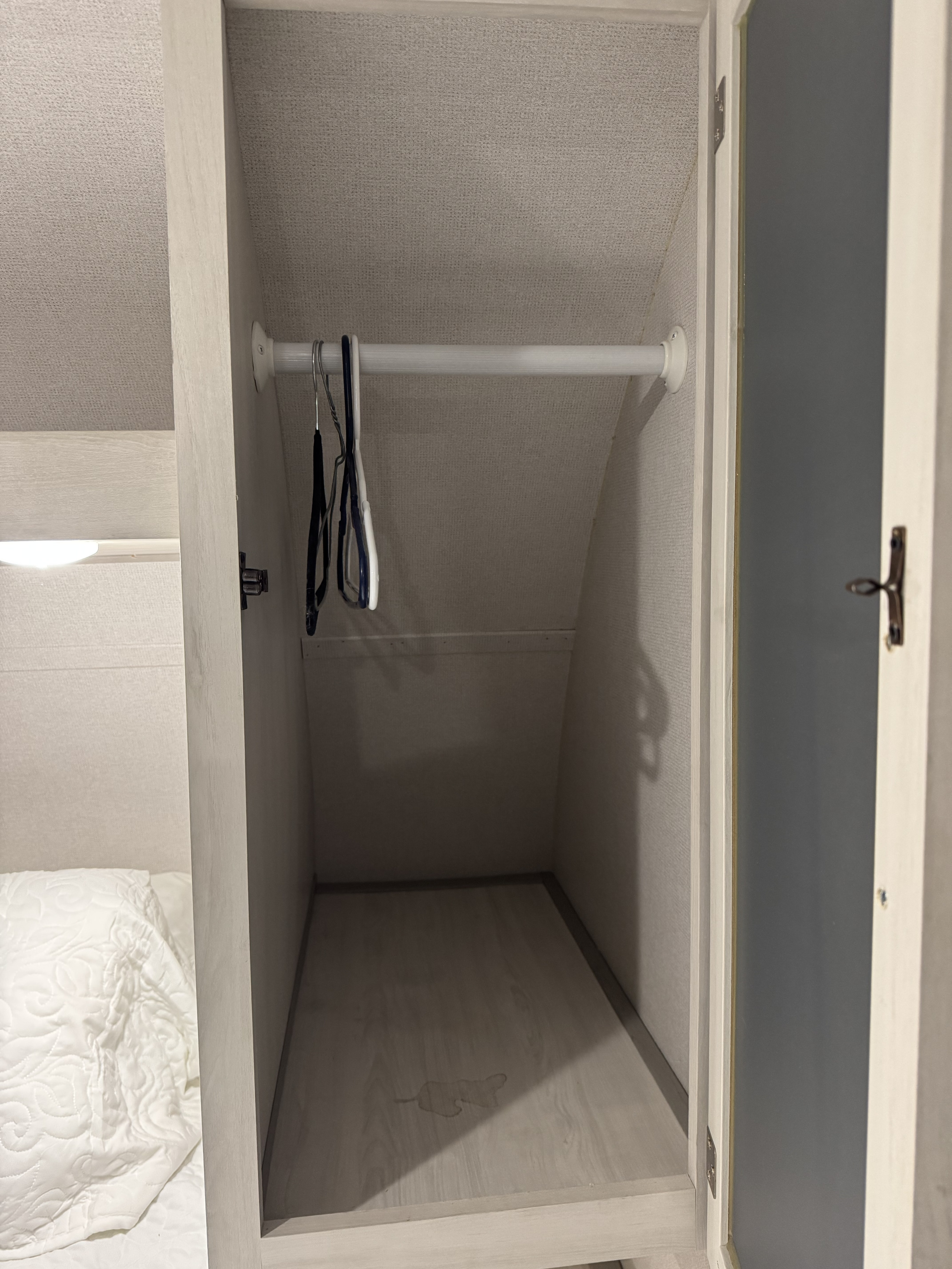 Open closet with hangers & hanging rod in an RV rental. Features light wood interior, textured walls, a floor stain, and a bed to the left.. Forest River Tracer 2021