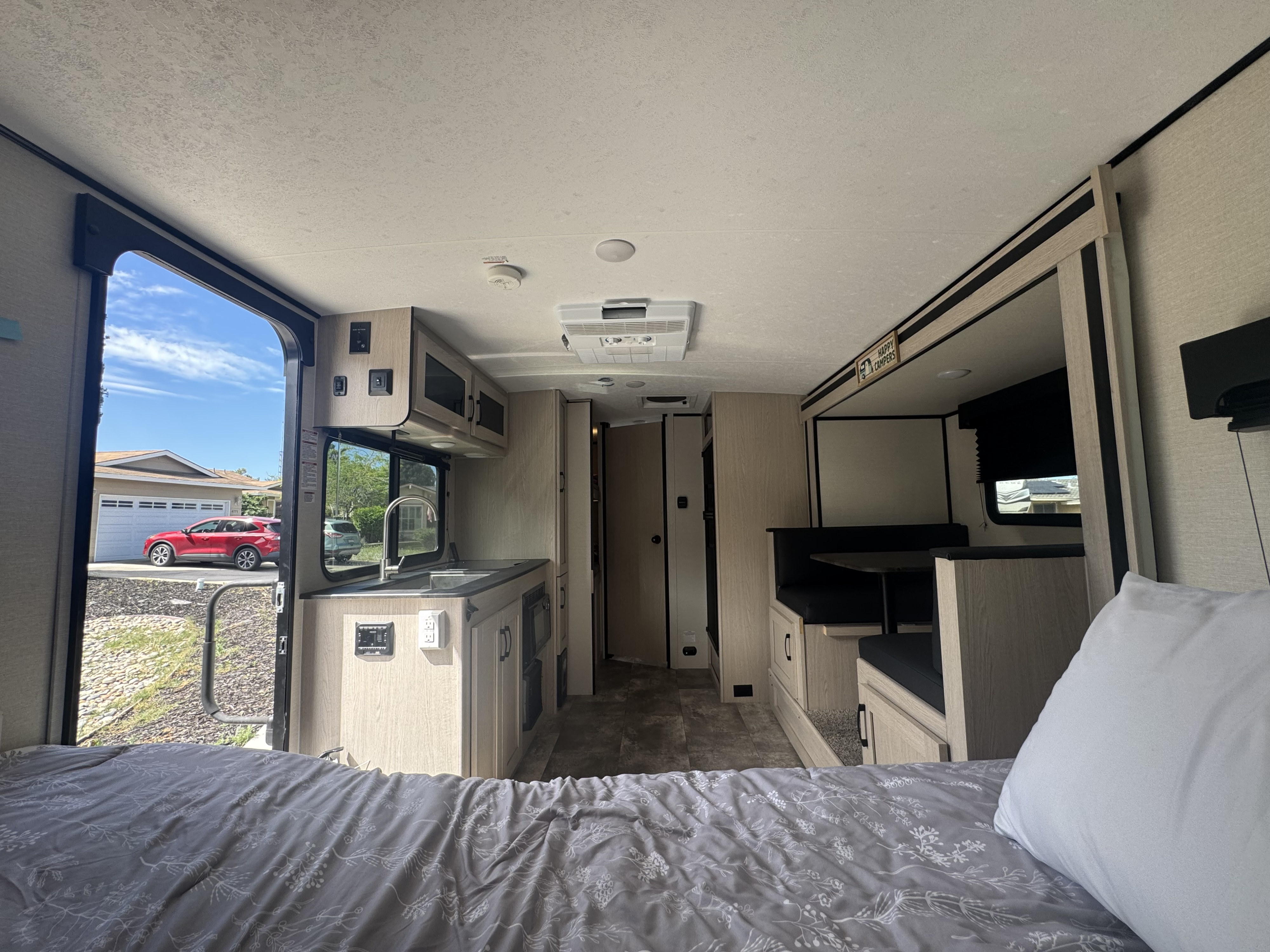 RV rental with modern interior: bed in foreground, kitchen, dinette, and open door showing outside. Light wood and black accents.. Coachmen Apex Nano 2023