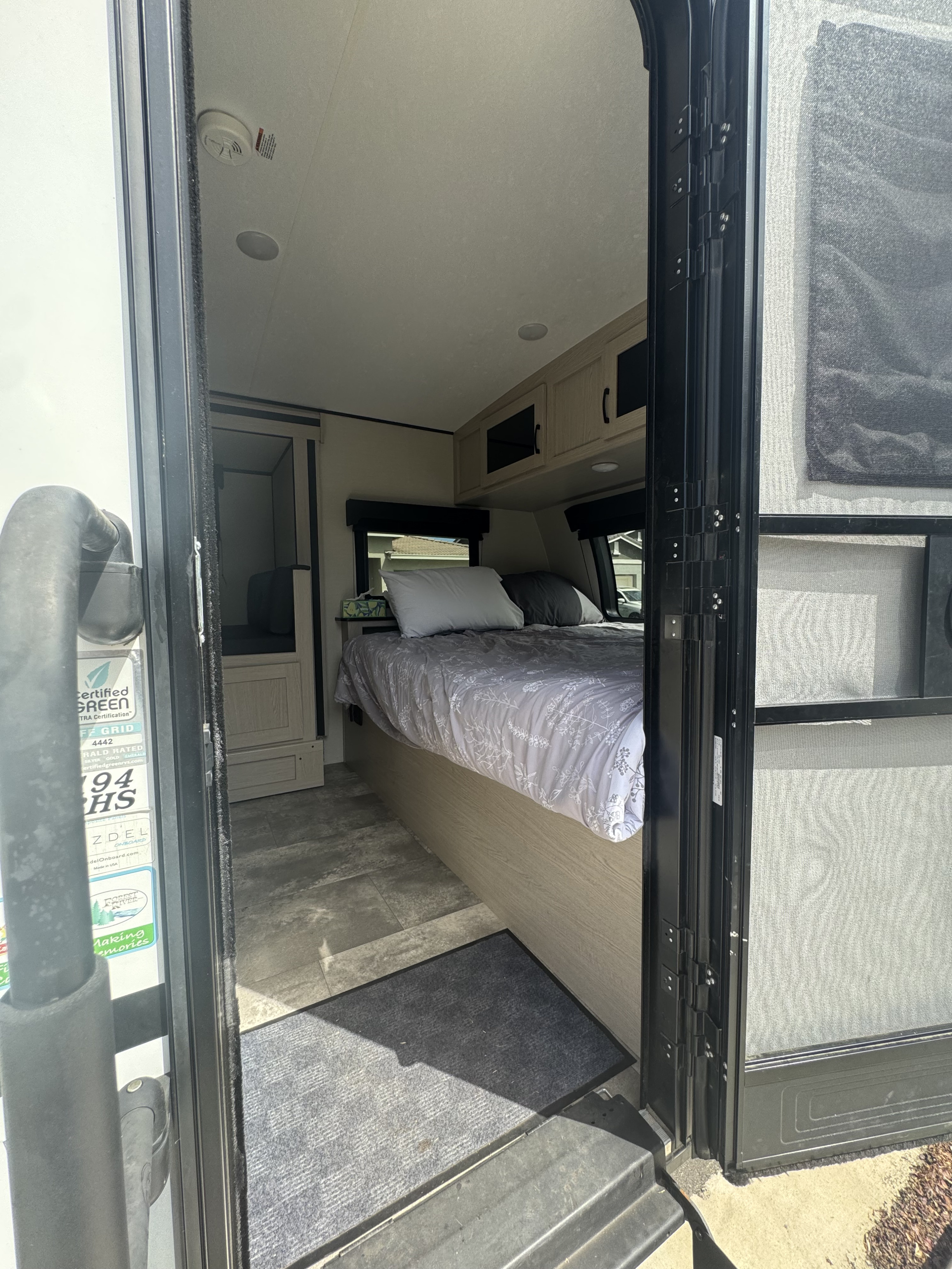 A cozy RV rental bedroom interior with a bed, overhead cabinets, and a smoke detector, seen from the open doorway.. Coachmen Apex Nano 2023