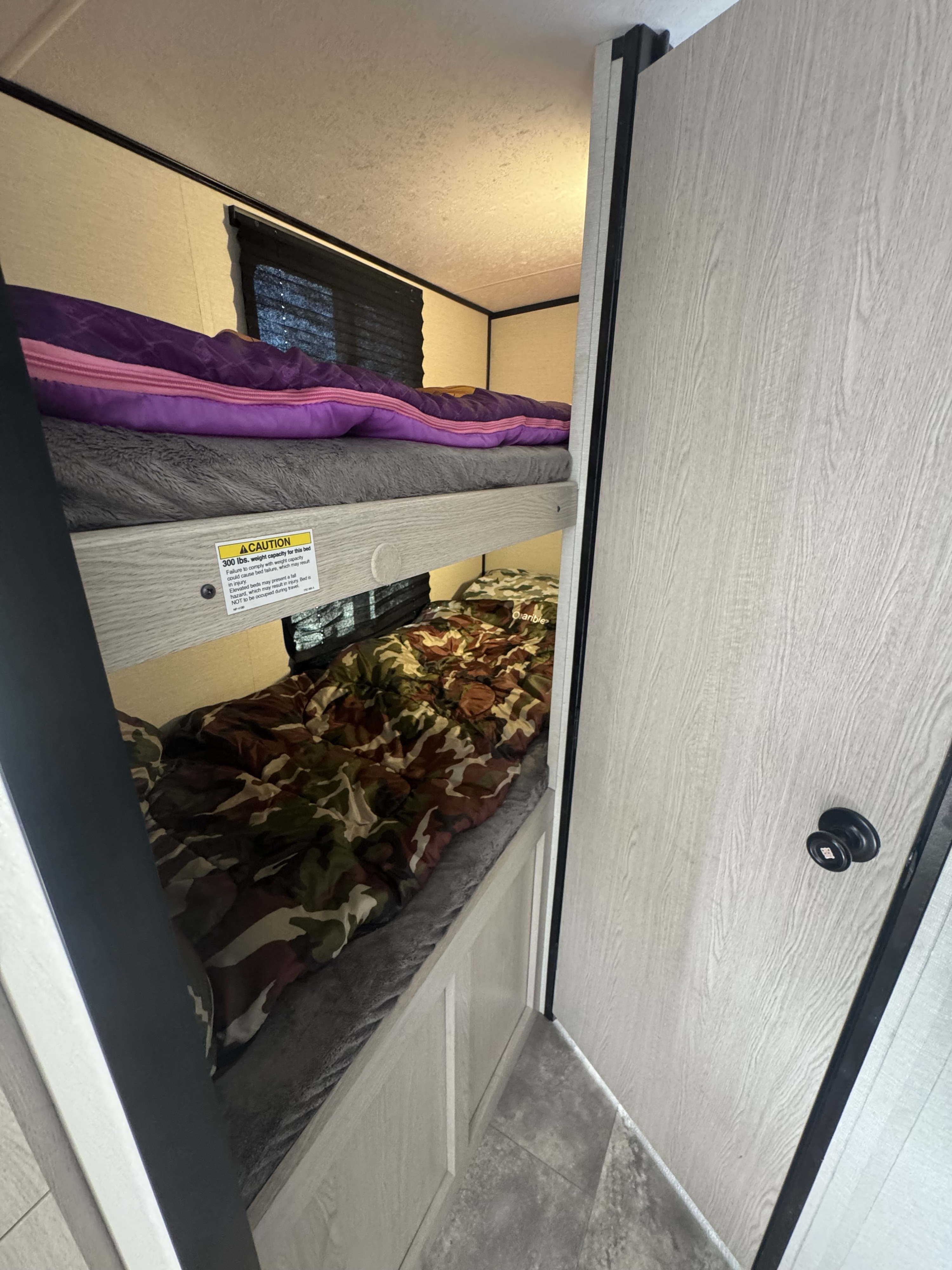 RV rental: Bunk beds inside camper. Top bunk has purple sleeping bag (300 lbs capacity); bottom has camouflage.. Coachmen Apex Nano 2023
