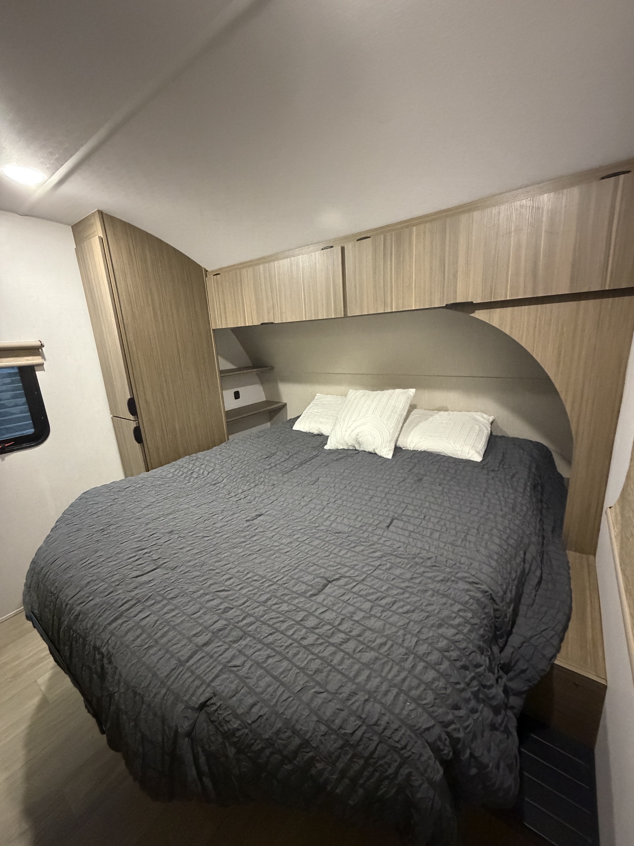 Inside this RV rental, a comfy bedroom offers a large bed with a gray quilted comforter, white pillows, and sleek wood storage cabinets.. Forest River Wildwood X-Lite 2025