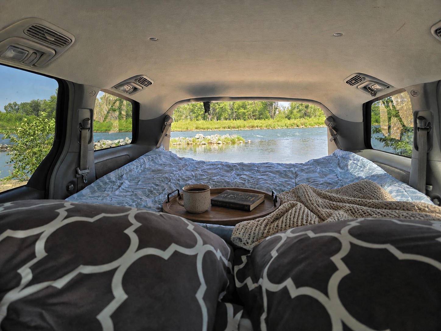 Cozy rv rental interior: A bed, coffee, and book with a scenic river view. Perfect for campervan travel.. Toyota Sienna 2007