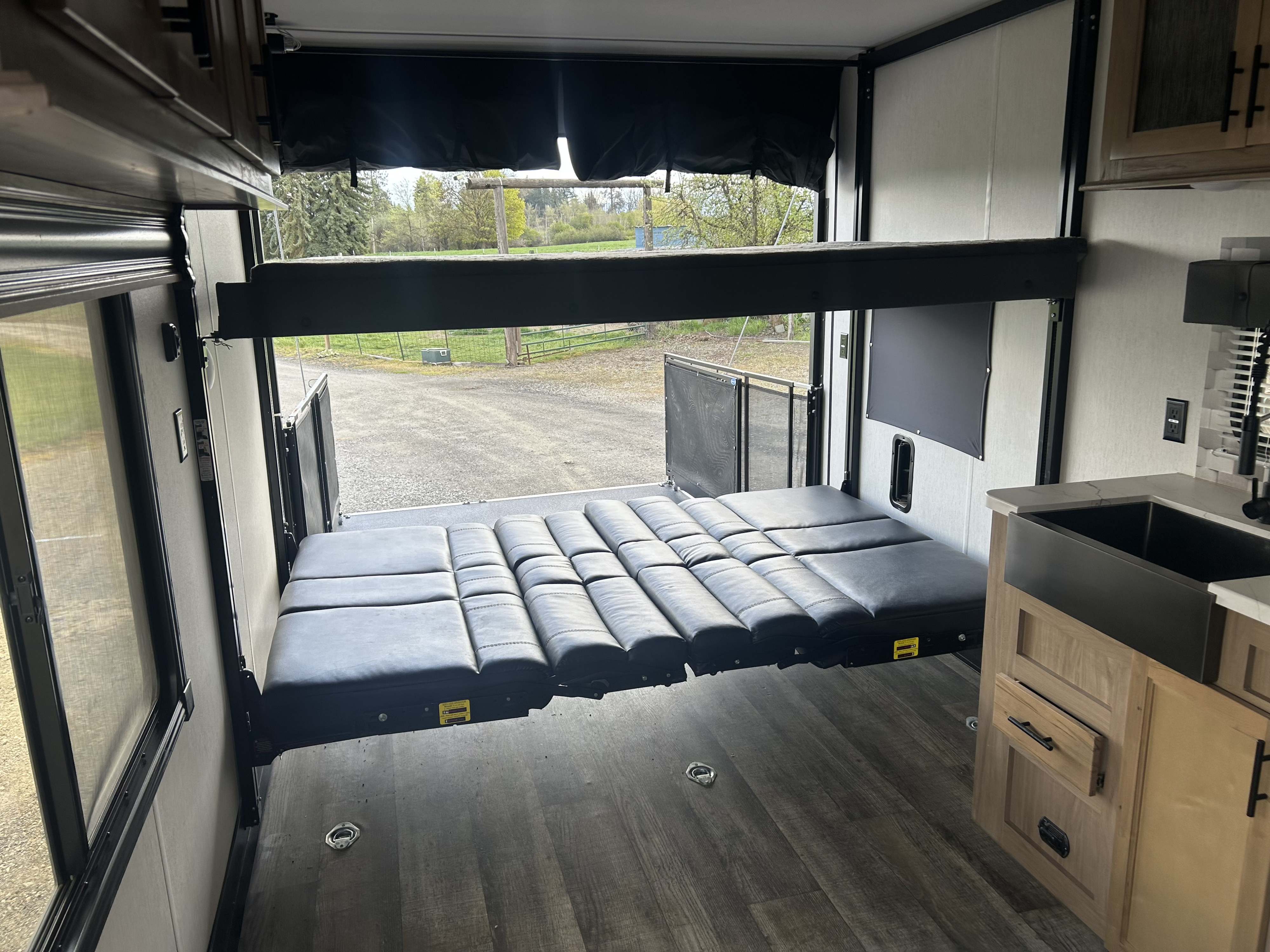 rv rental toy hauler interior. Convertible lower bed, upper bunk, and kitchenette on the right, with the rear ramp open.. Forest River Cherokee Wolf Pack 2023