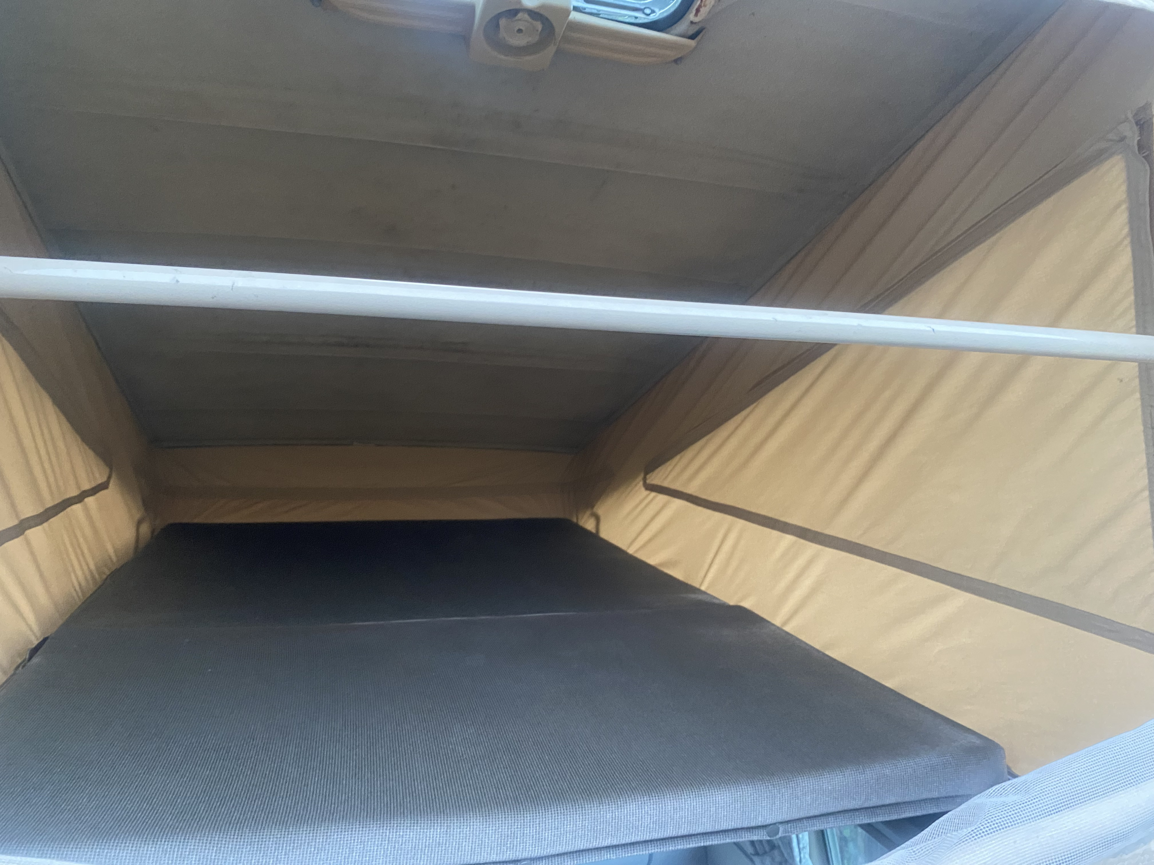 RV rental pop-top camper interior: elevated sleeping area with a gray textured mattress, tan fabric walls, and a white support bar.. Volkswagen T3 Westfalia 1988