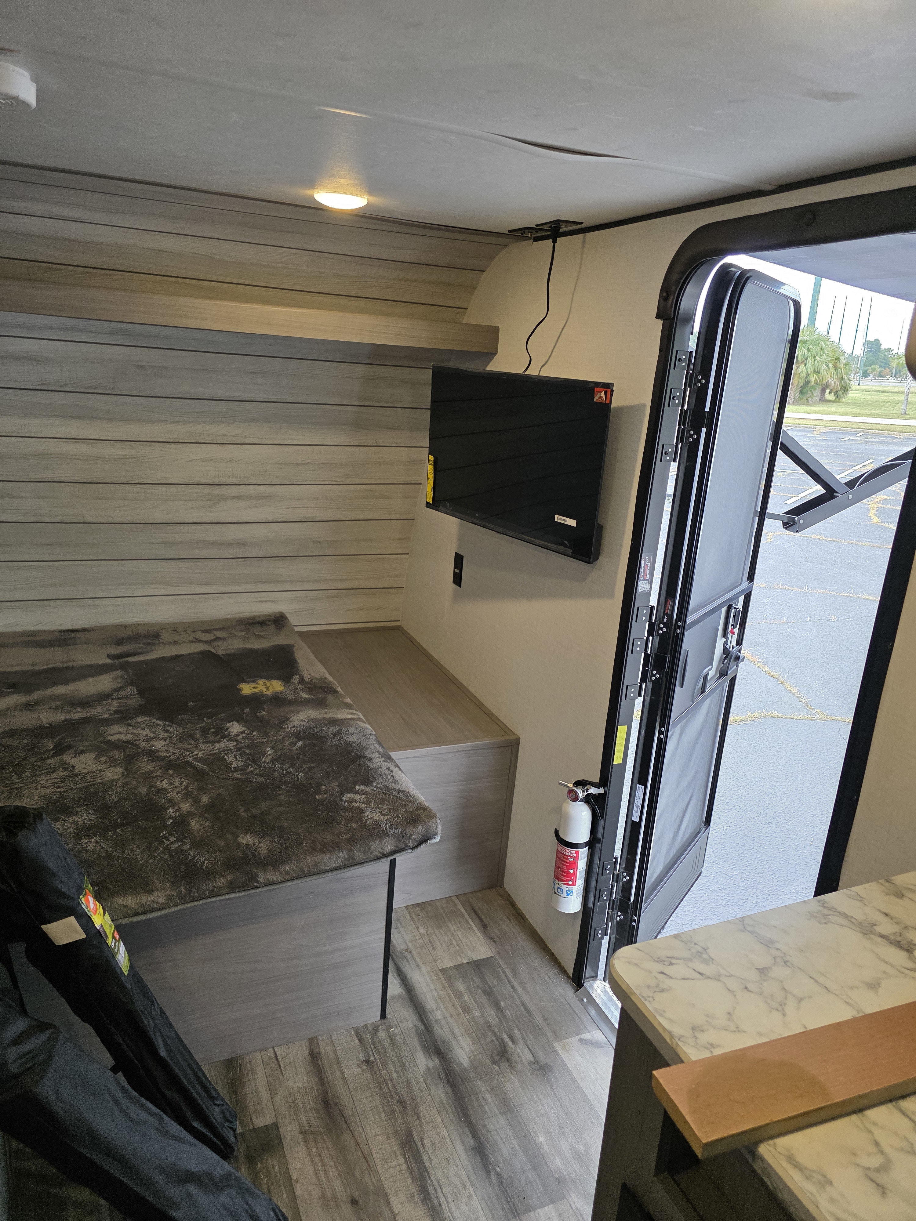 View inside an RV rental: bed, TV, open door, fire extinguisher, and wood-look walls/floor. Compact and functional.. Coleman Coleman Coleman Lantern Lt 17B 2024