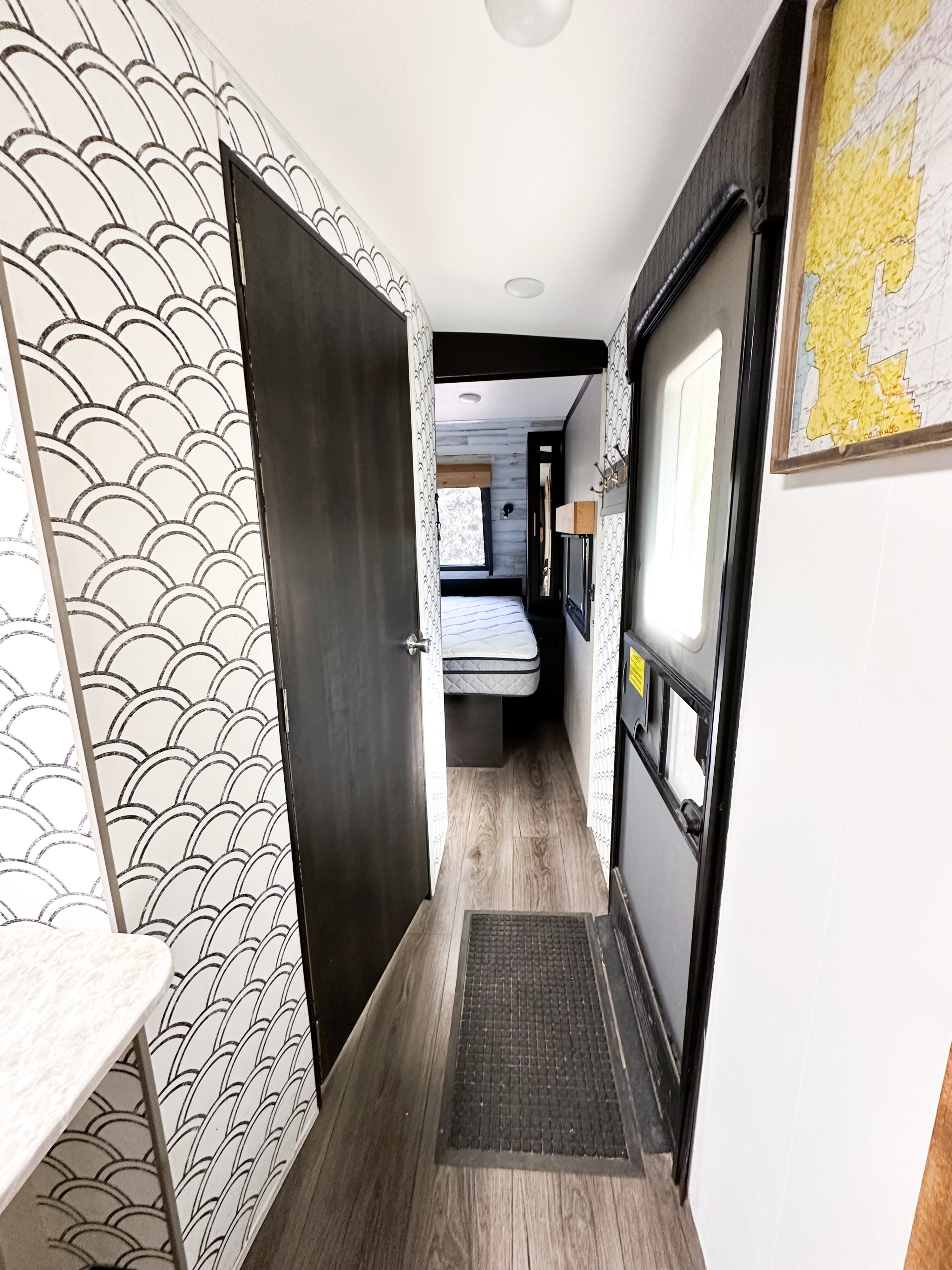 Modern RV rental interior hallway with scallop-patterned wallpaper, main entrance, a map, and a glimpse into a bedroom.. Jayco White Hawk 2021