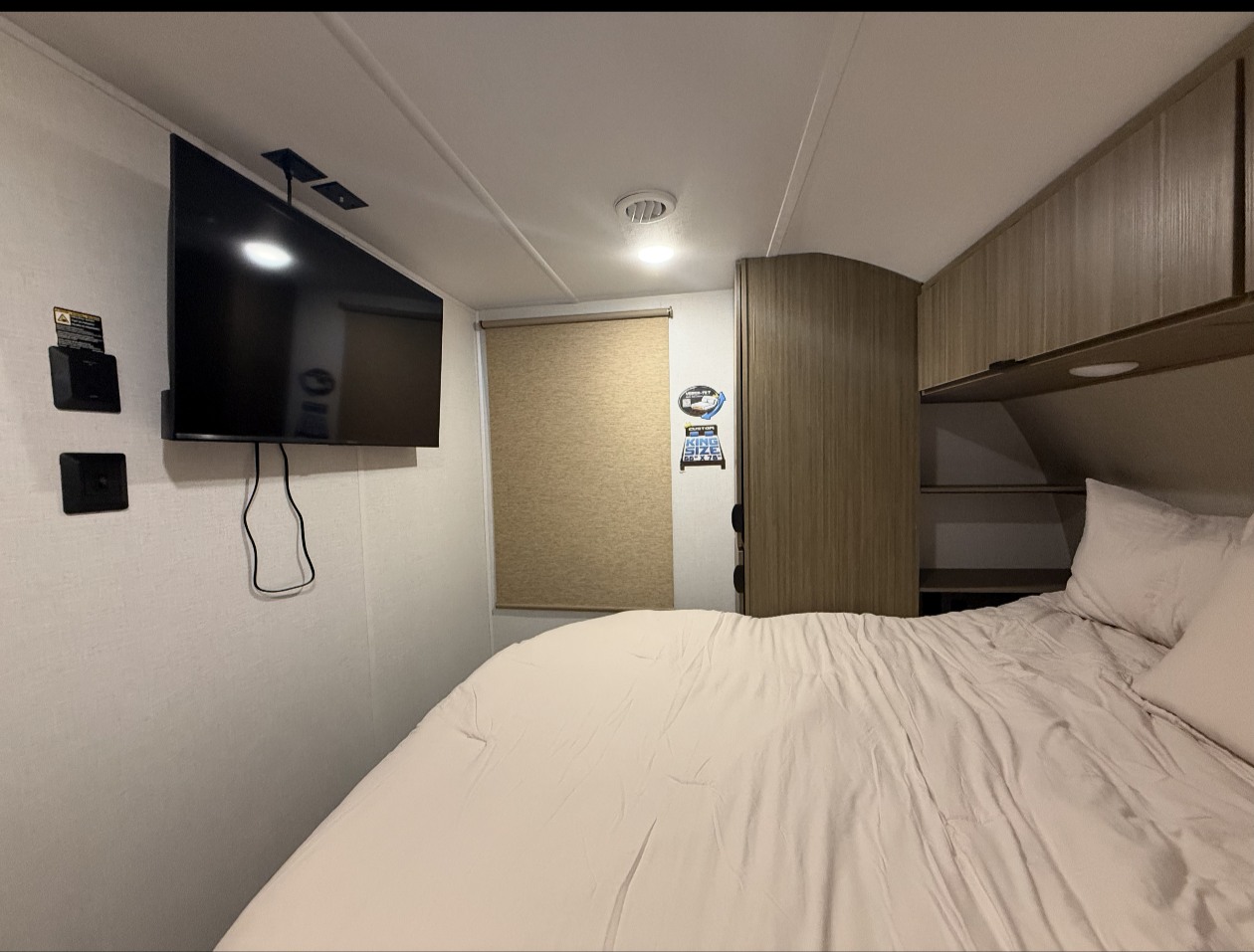 Cozy RV rental bedroom features a mounted TV, comfortable bed with light sheets, and convenient overhead storage.. Forest River Salem 2025