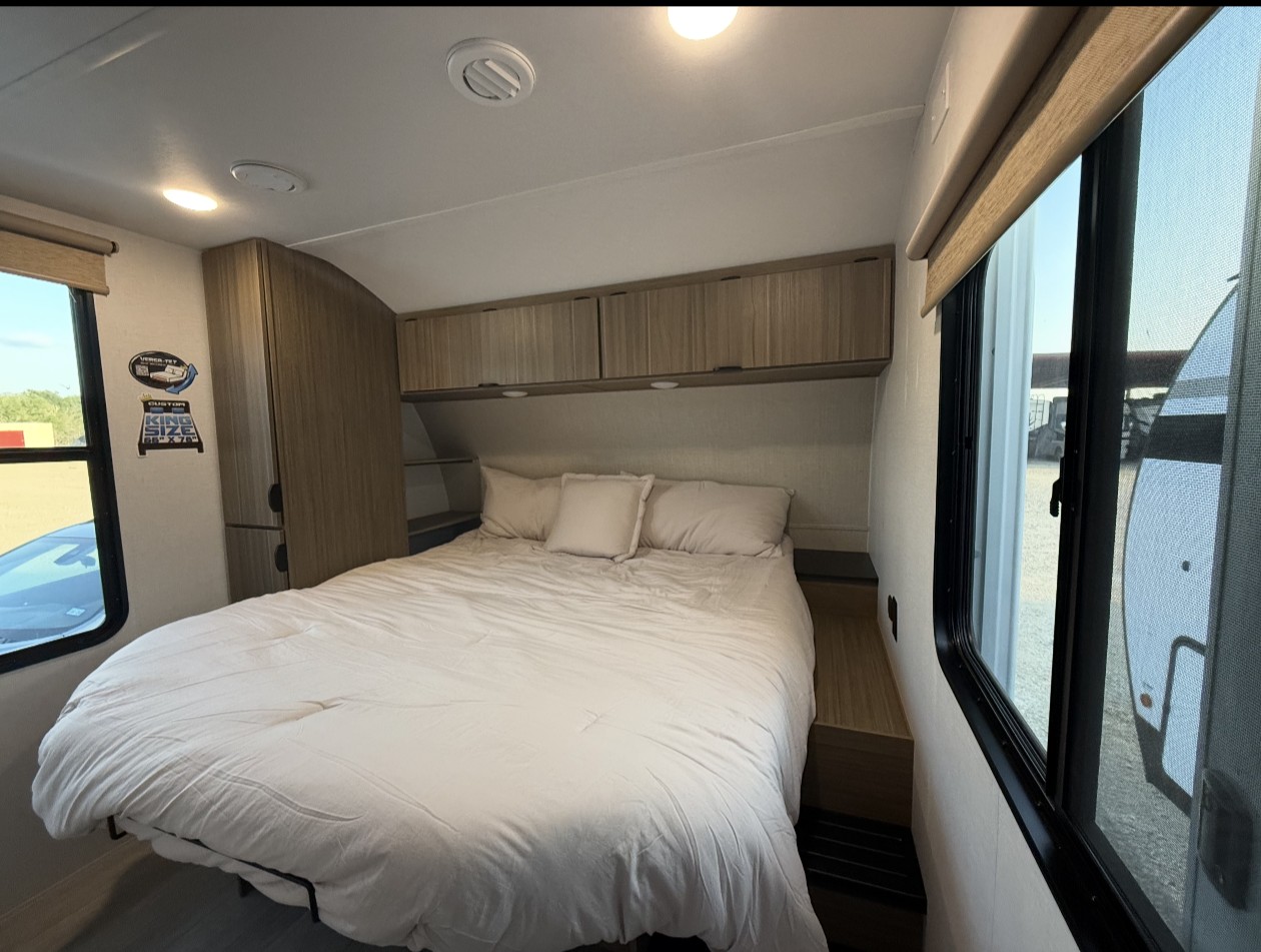 Inside a modern RV rental bedroom with a comfortable king bed, wood storage, and bright windows on both sides.. Forest River Salem 2025