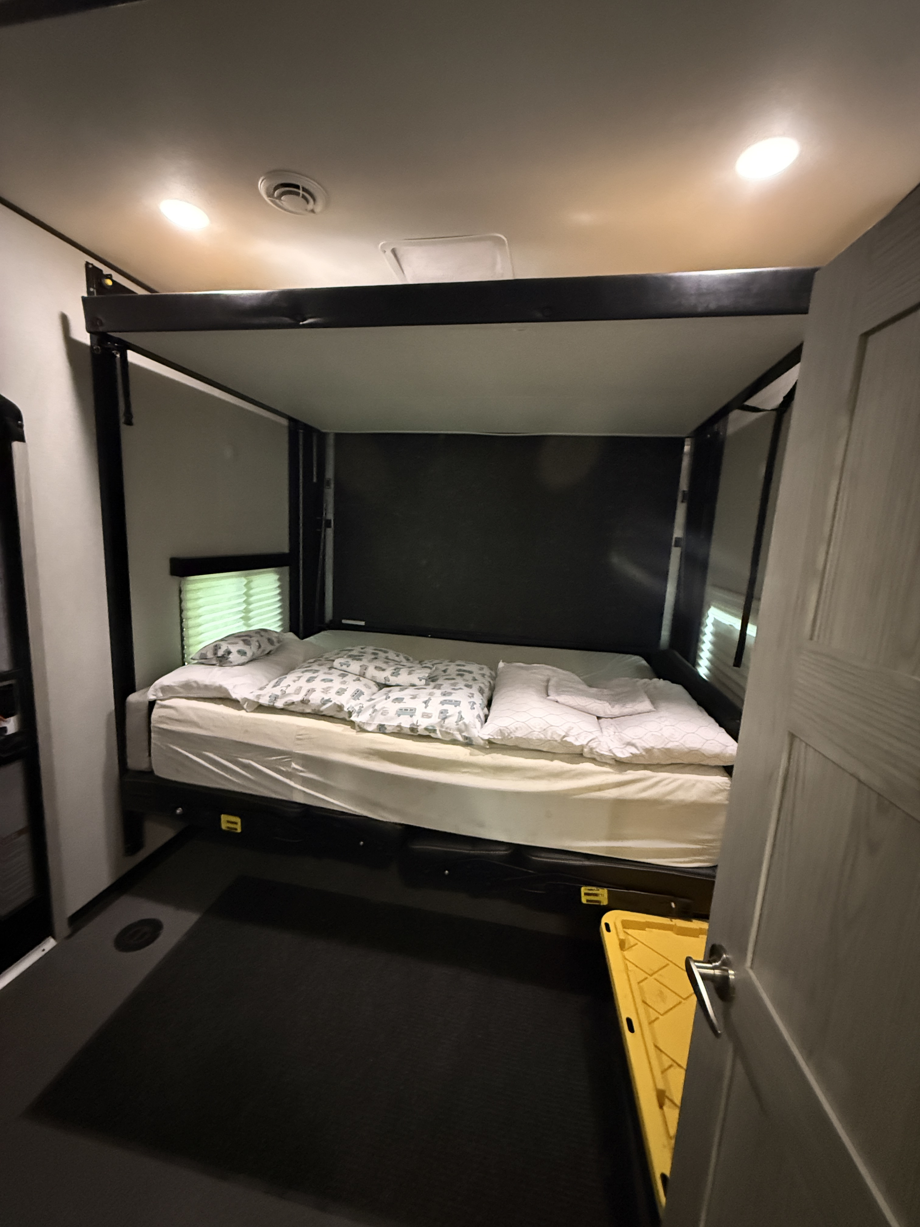 Inside an RV rental: a cozy bedroom features a lifting bed, window, and bright overhead lights for comfortable travel.. Keystone RV Fuzion Impact Vapor Lite Toy Hauler 2022
