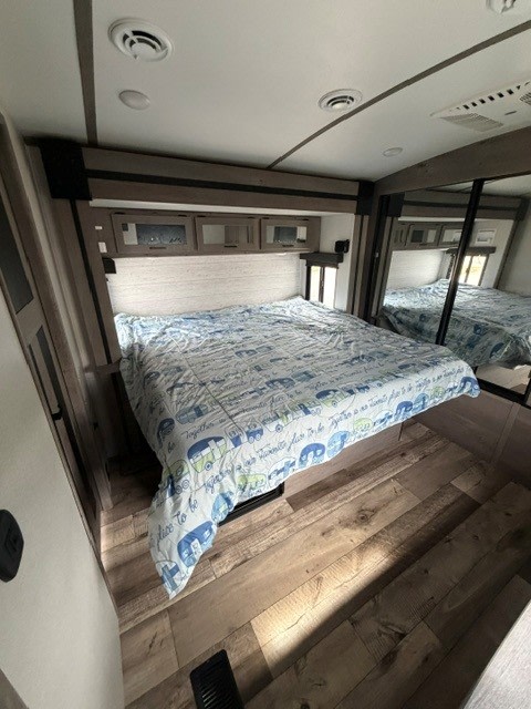 Cozy RV rental bedroom: queen bed with camper quilt, wood floor, overhead cabinets, and mirrored wardrobe for space-saving storage.. Keystone RV Outback 2021