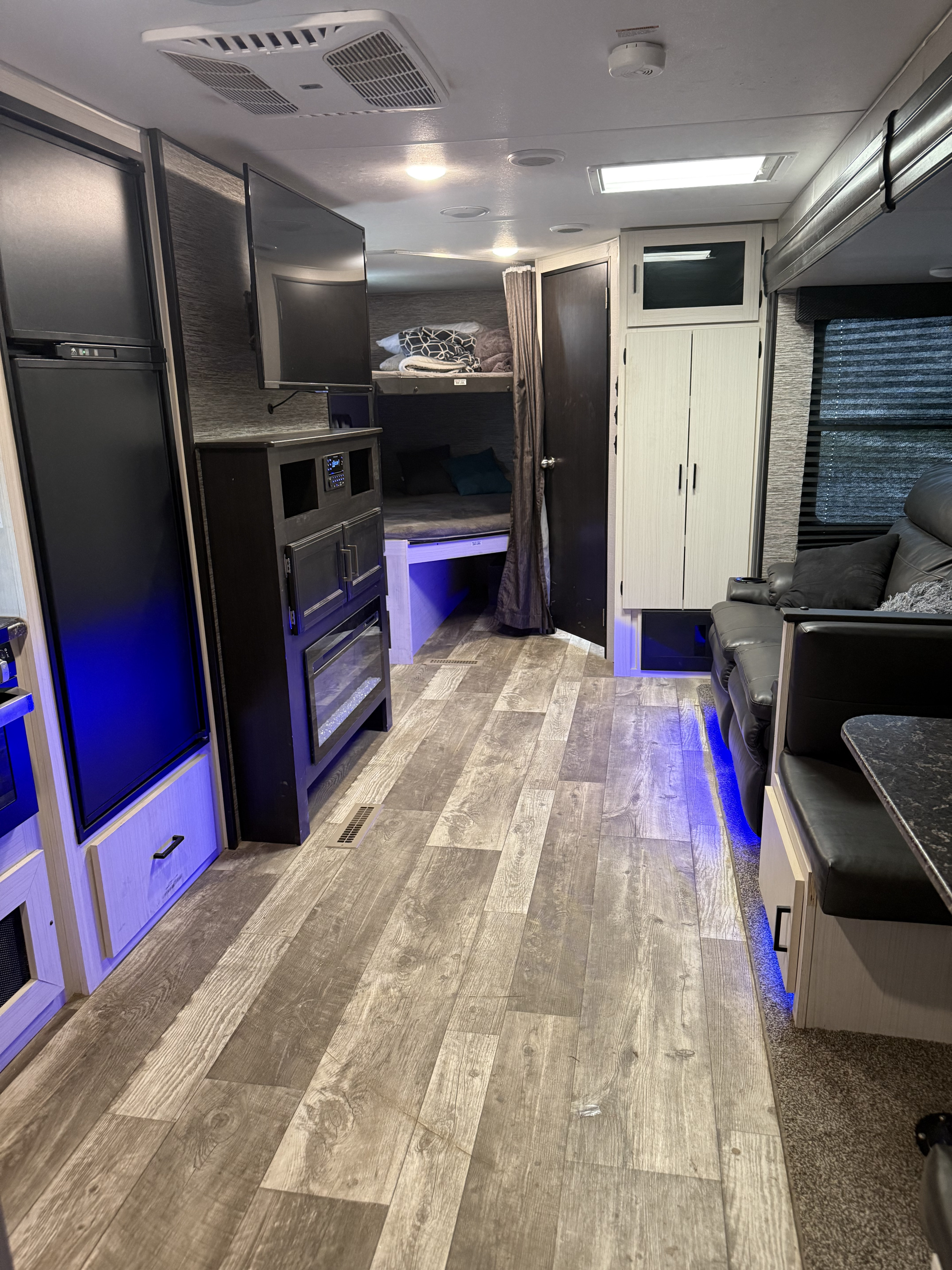 Interior of an rv rental: Bunk beds, entertainment center with fireplace, fridge, and seating area with blue accent lights.. Venture Stratus 2021