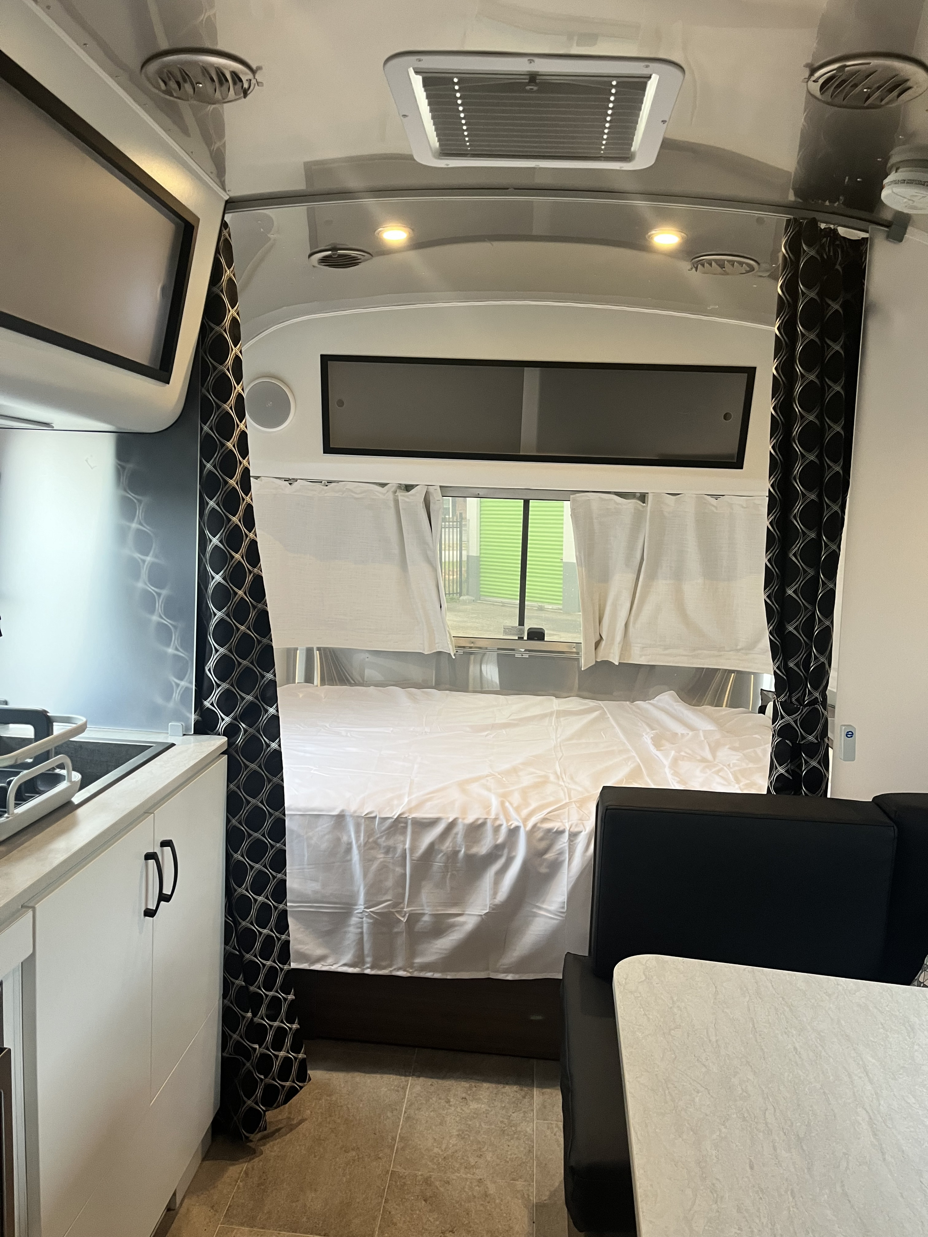 Interior of an RV rental featuring a cozy bedroom, kitchenette, and dining area with stylish black curtains.. Airstream Caravel 2024