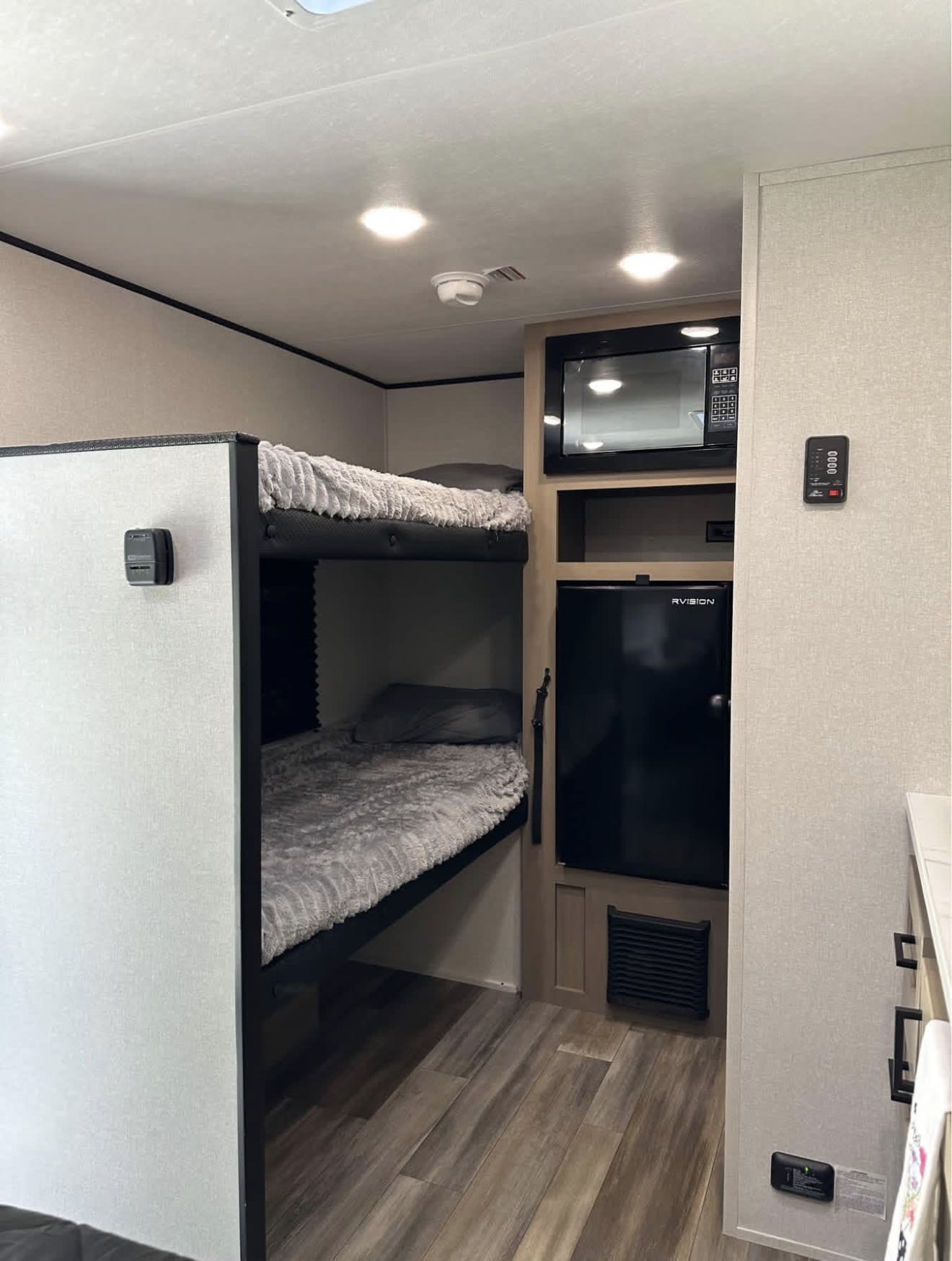 Inside an RV rental: two bunk beds with gray bedding, microwave, and mini-fridge in a compact, modern space.. Highland Ridge RV Colt 2026