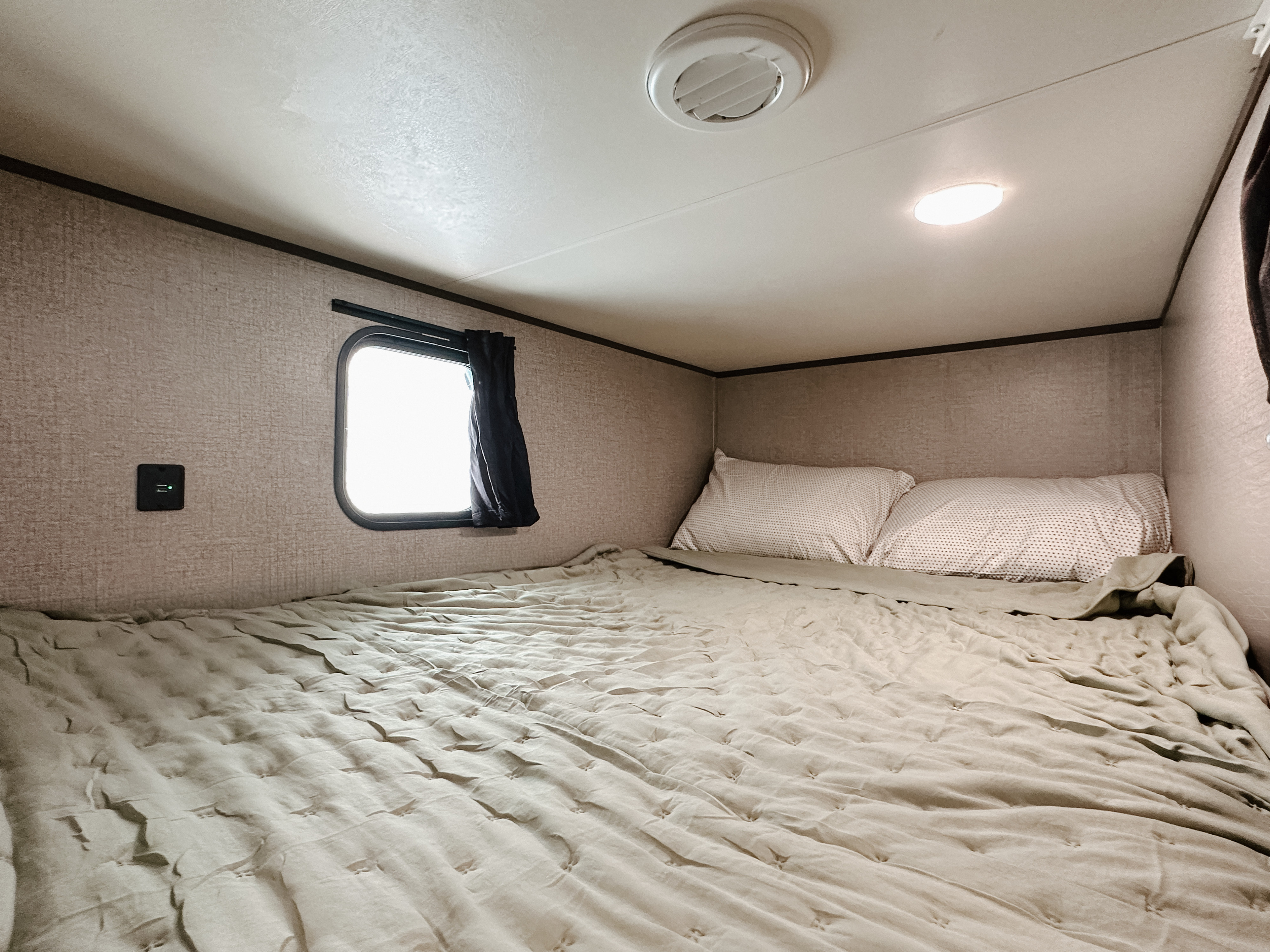 Compact RV rental sleeping area featuring a bed with quilt, window, USB charging port, ceiling vent, and light.. Jayco Jay Flight SLX 2021