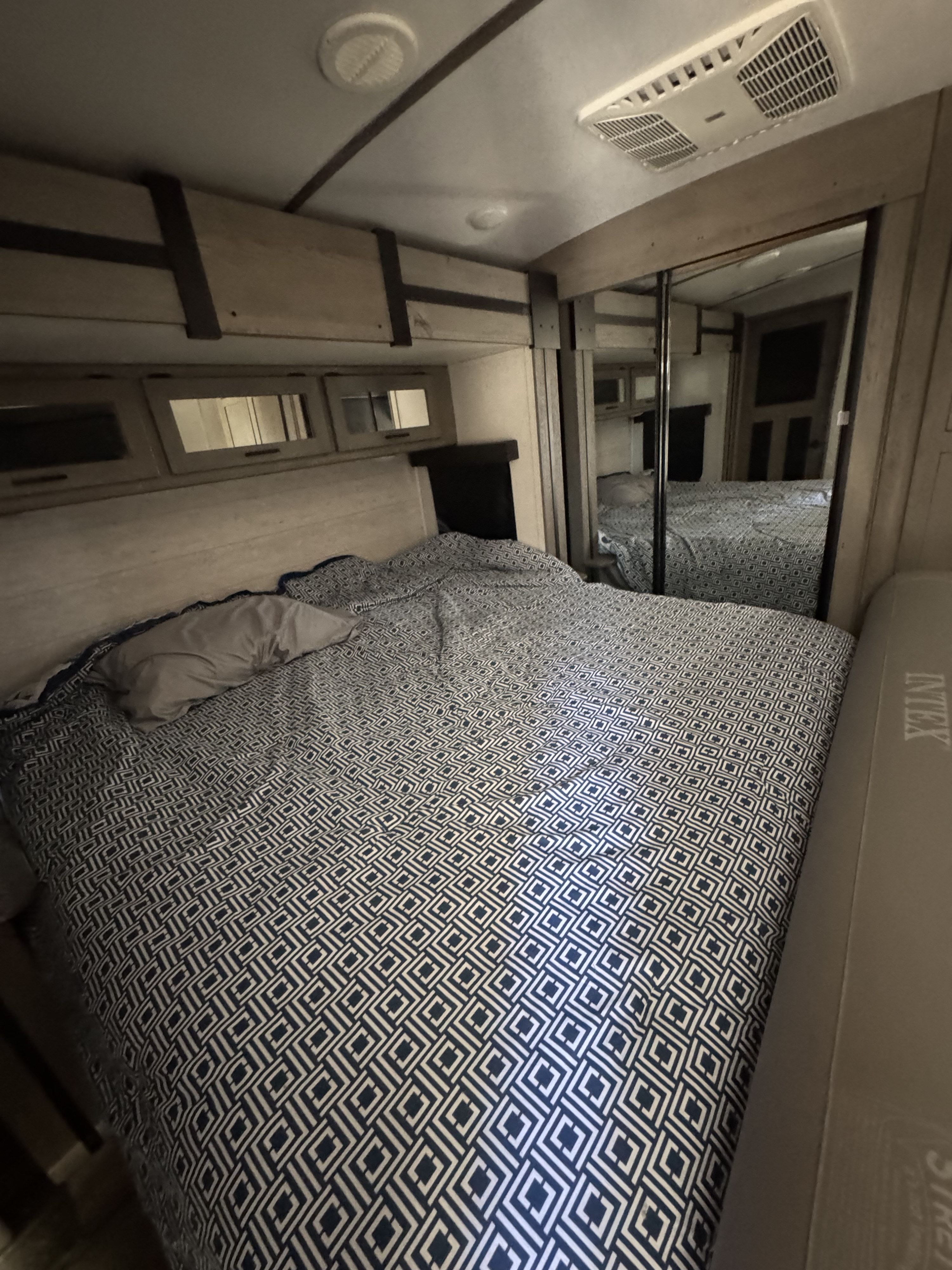 Cozy RV rental bedroom featuring patterned bedding, overhead storage, and mirrored closet doors.. Keystone RV Outback 2021