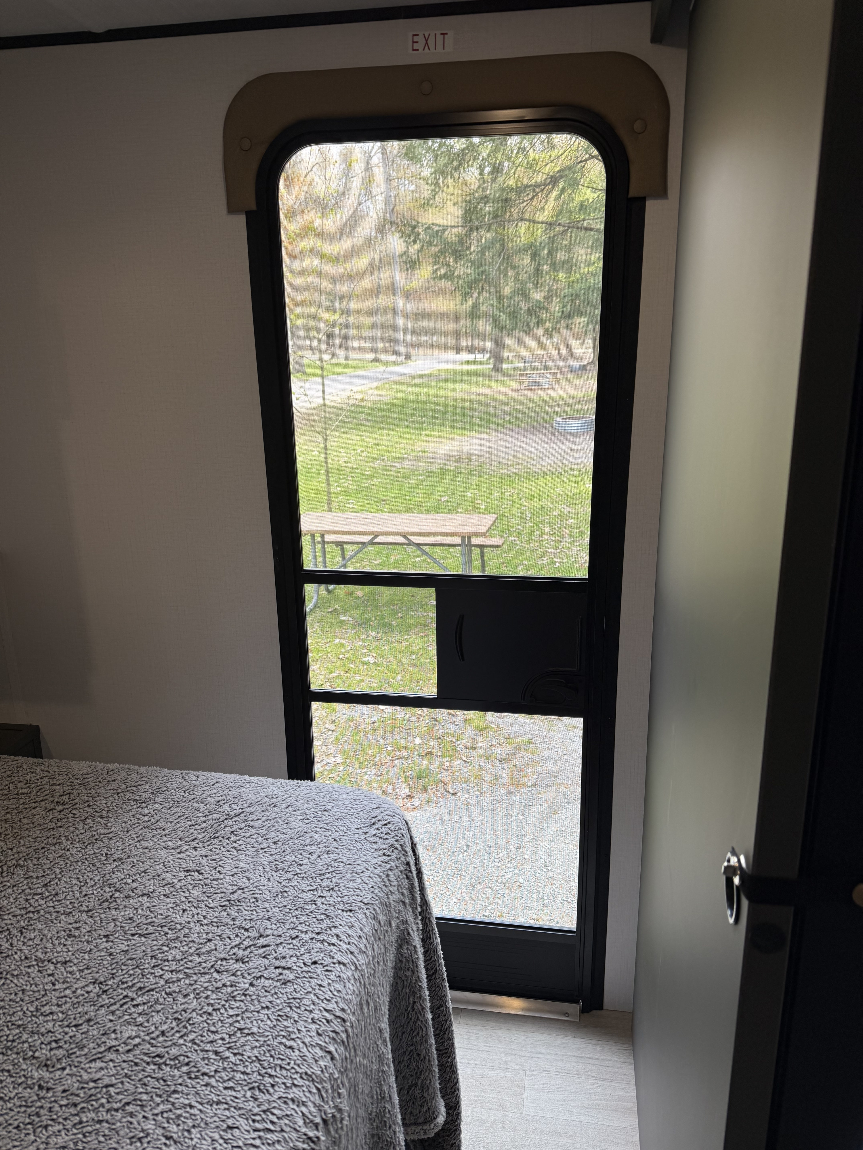 Inside an rv rental, a bedroom offers a screened door view of a picnic table and fire pit at a campground.. Keystone RV Bullet 21RKC 2026