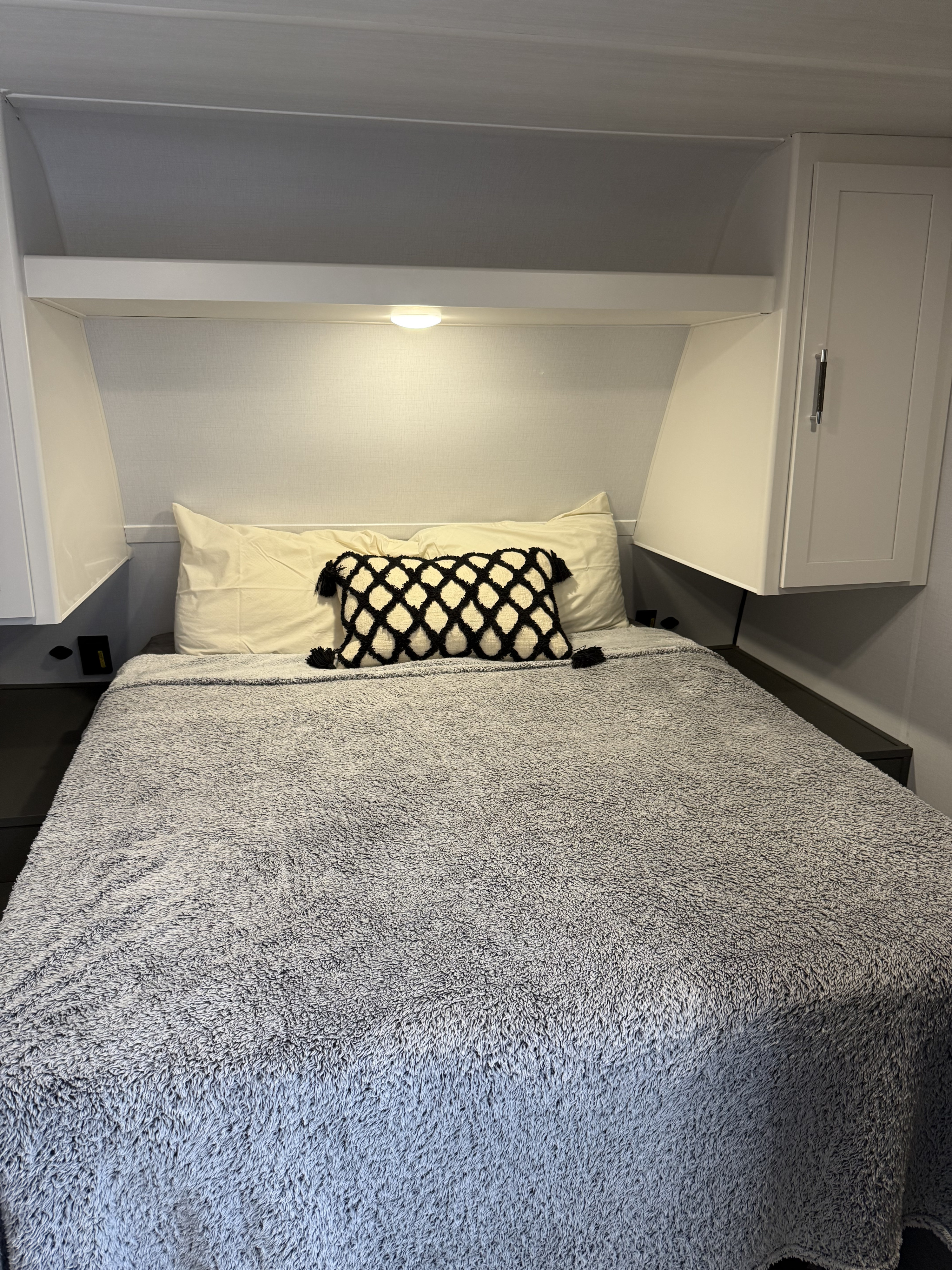 Cozy bed in an RV rental, with a fluffy grey blanket, decorative pillow, and practical overhead storage for travelers.. Keystone RV Bullet 21RKC 2026