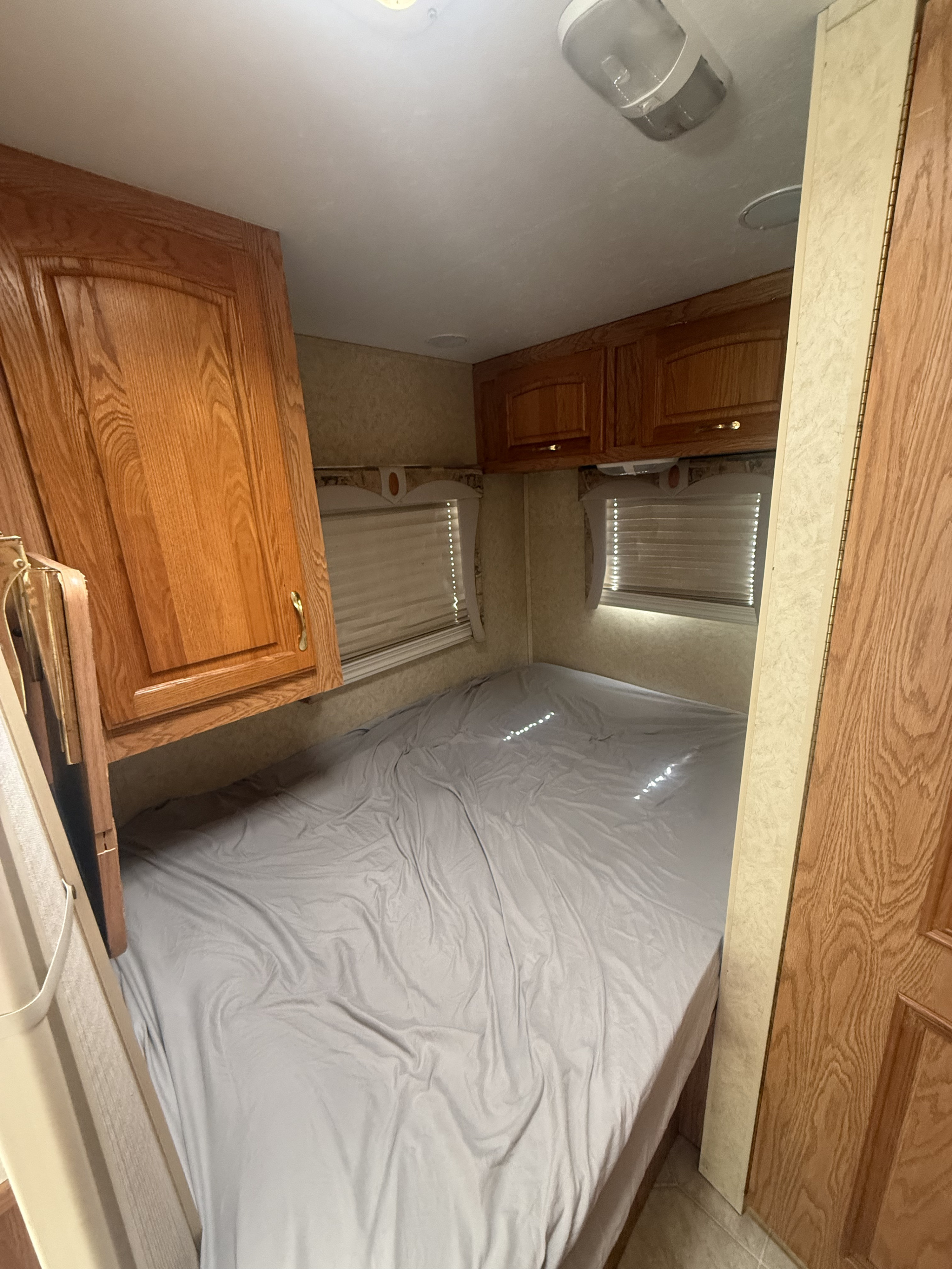 This RV rental bedroom offers a comfortable bed with grey sheets, overhead wooden cabinets, and window blinds for your trip.. Jayco Escapade 2005